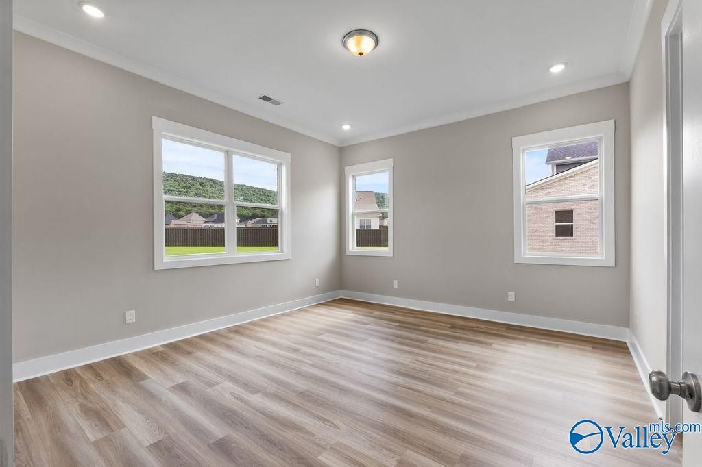 Bright secondary bedroom with gray walls, large windows overlooking woods, and LVP flooring in Evermore Homes The Oxford, Owens Cross Roads