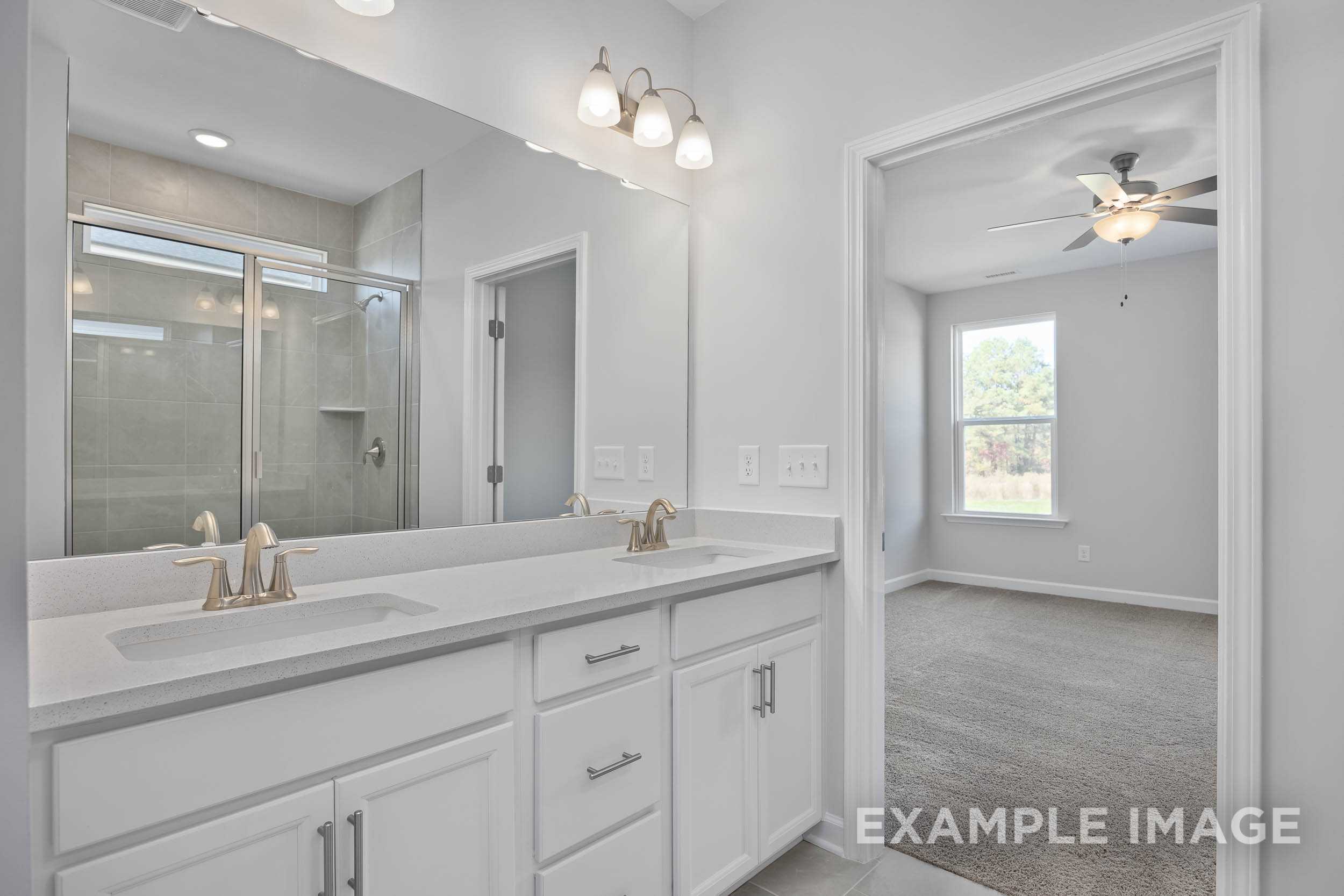 Master bathroom in The Ash by Davidson Homes featuring white double vanity, frameless glass shower, and adjacent carpeted bedroom