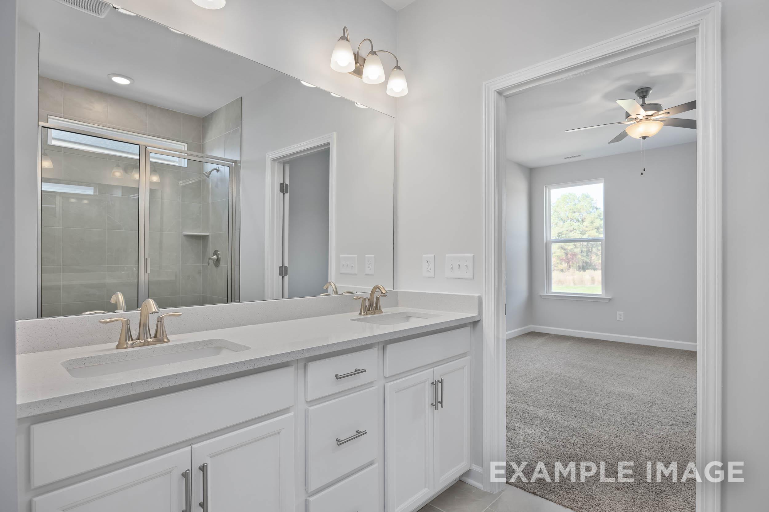 Master bathroom in The Ash by Davidson Homes featuring white double vanity, frameless glass shower, and adjacent carpeted bedroom