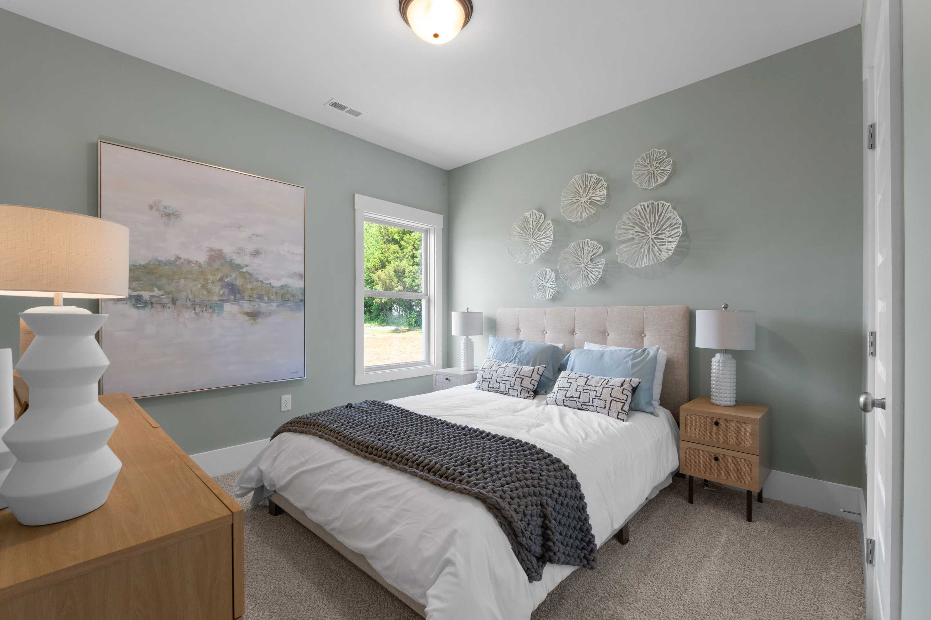 Serene bedroom at Hollon Meadow in Decatur AL with light blue walls, tufted bed, abstract art, and window view