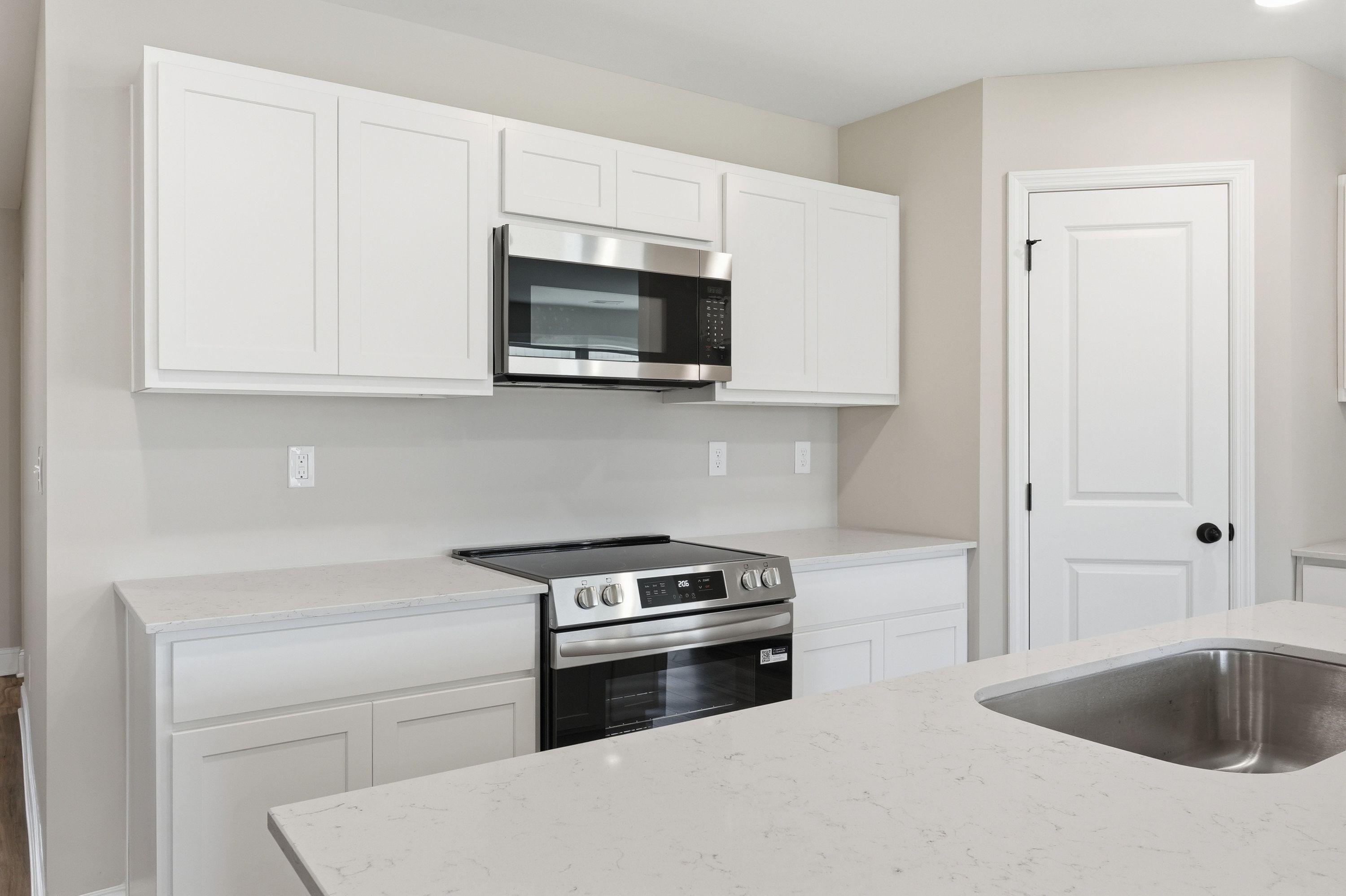 Spacious kitchen in The Daphne V by Davidson Homes featuring white shaker cabinets, stainless steel appliances, and quartz counters