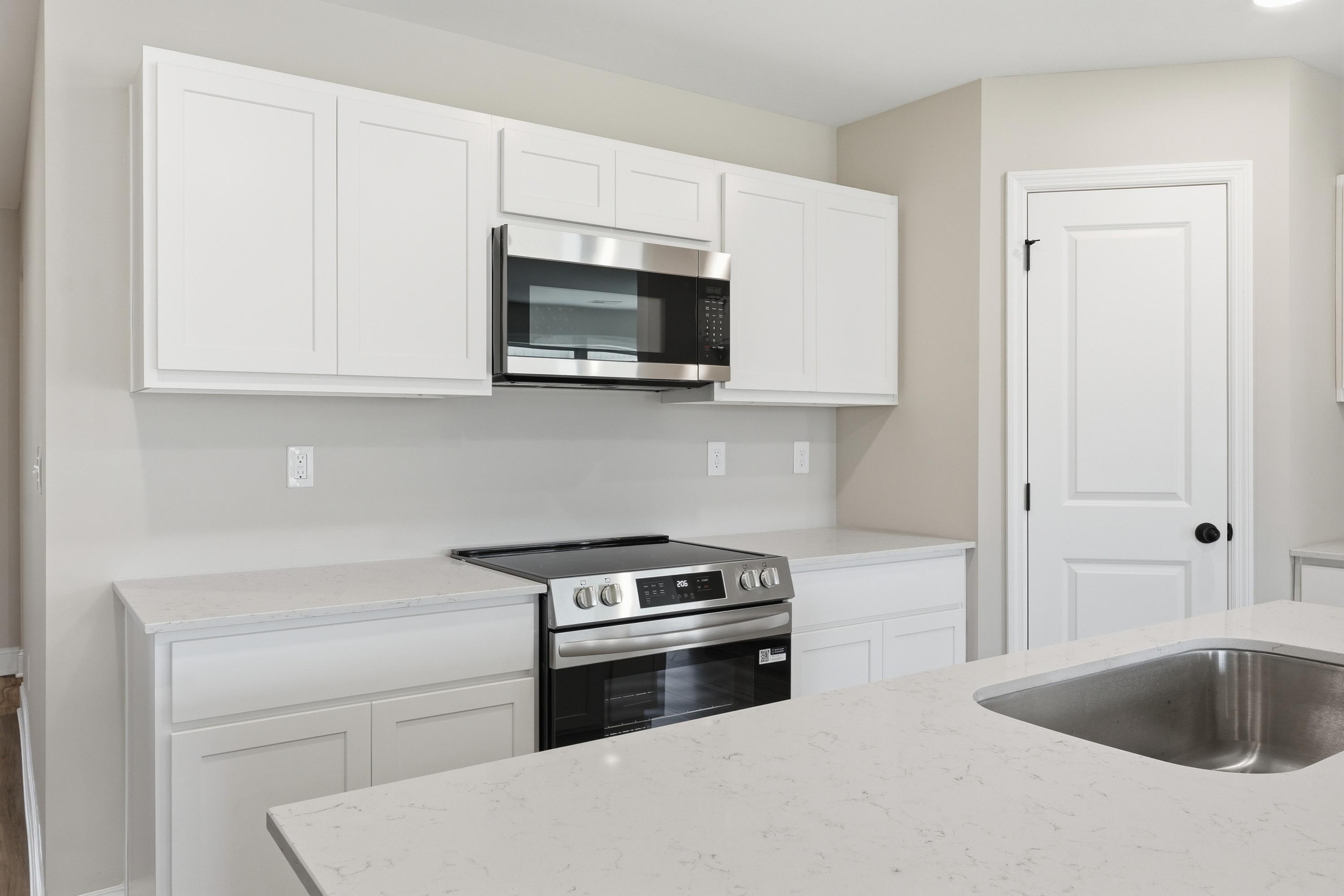 Spacious kitchen in The Daphne V by Davidson Homes featuring white shaker cabinets, stainless steel appliances, and quartz counters