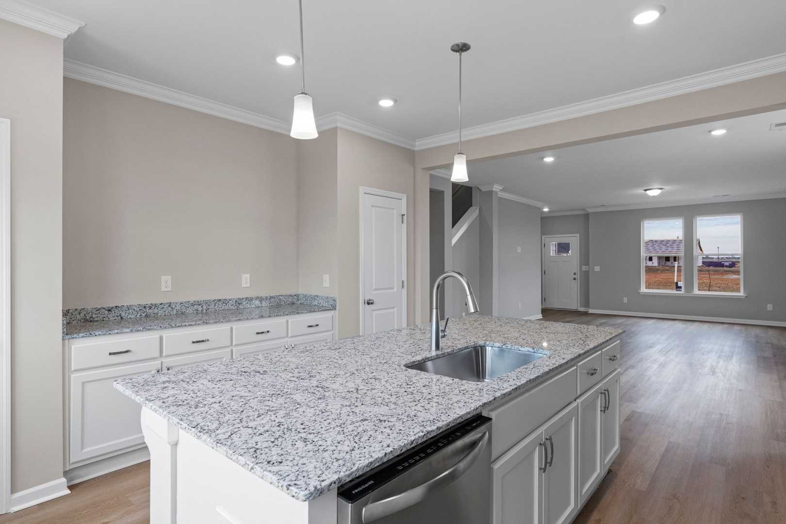 Open-concept kitchen in The Stella showcasing white cabinets, granite island with sink, and hardwood floors