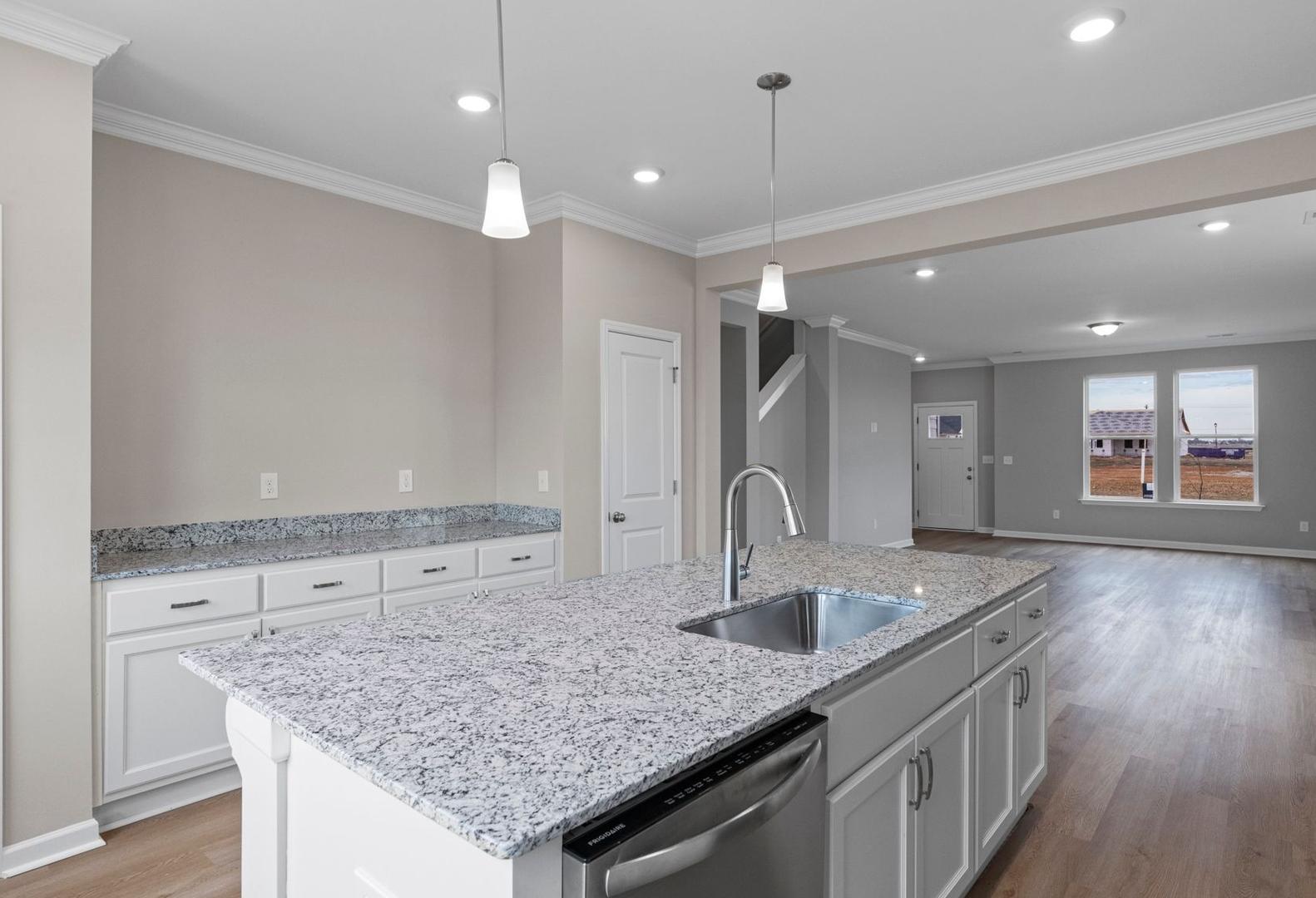 Spacious kitchen in The Stella A with white cabinets, granite island, stainless sink, and open layout to living area