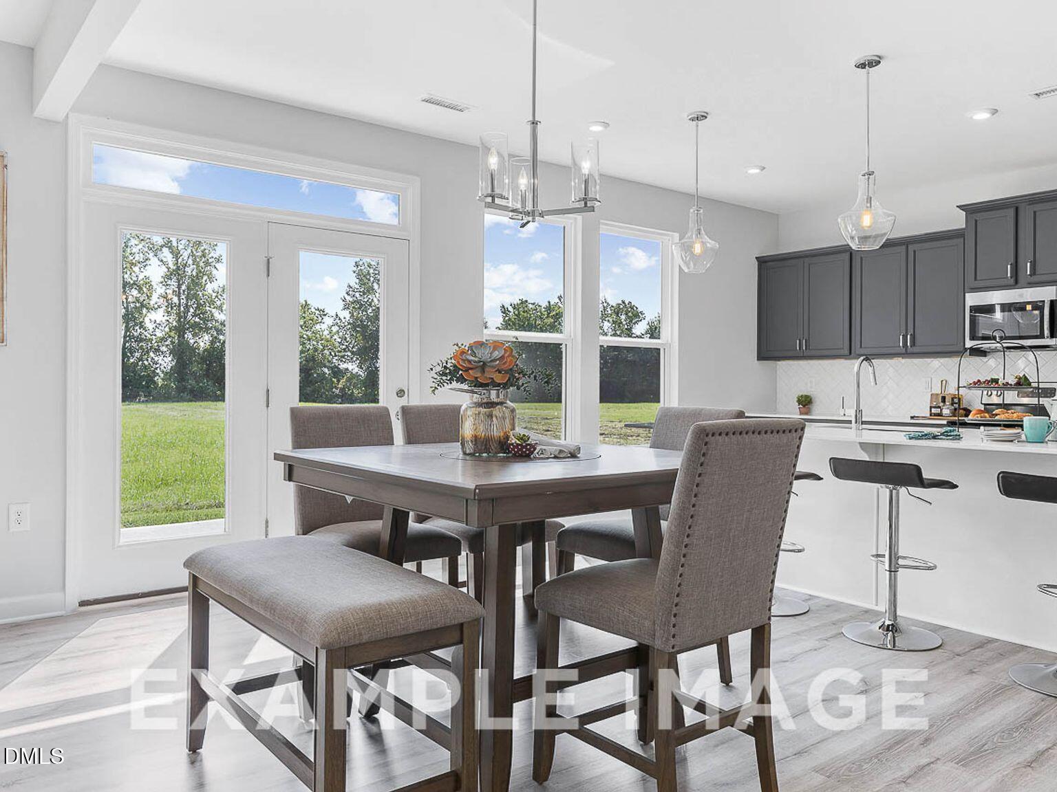 Bright dining area with wooden table, upholstered chairs, and bench overlooking green fields through French doors in Lillington home