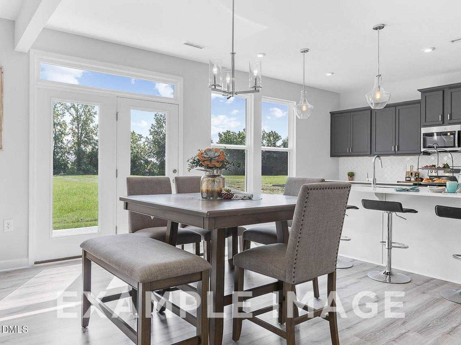 Open-concept kitchen and dining area with gray cabinets, wooden table, and backyard views in Davidson Homes Chestnut B, Lillington, NC
