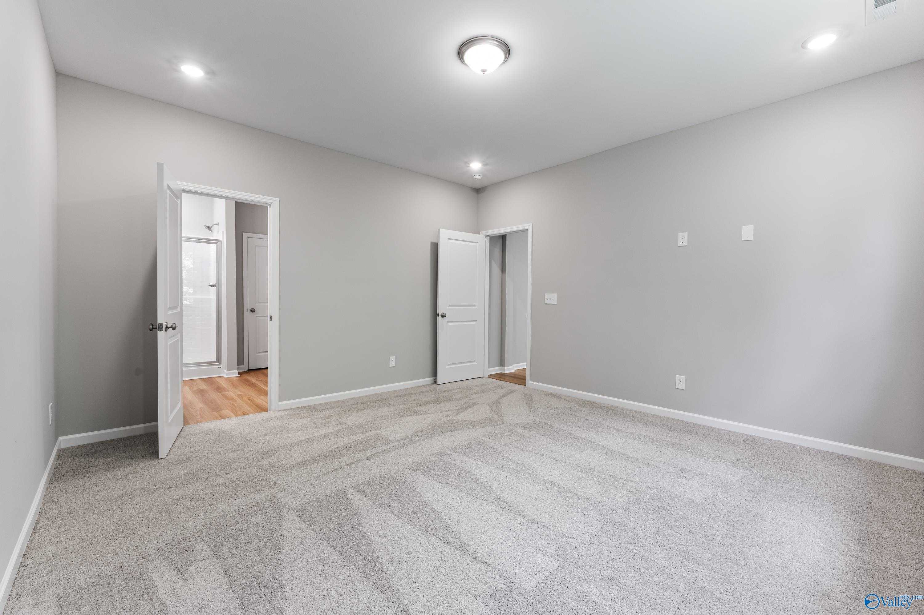 Bright bedroom with gray walls, plush carpet, recessed lights, and doors to bathroom and closet in Davidson Homes The Phoenix, Hazel Green