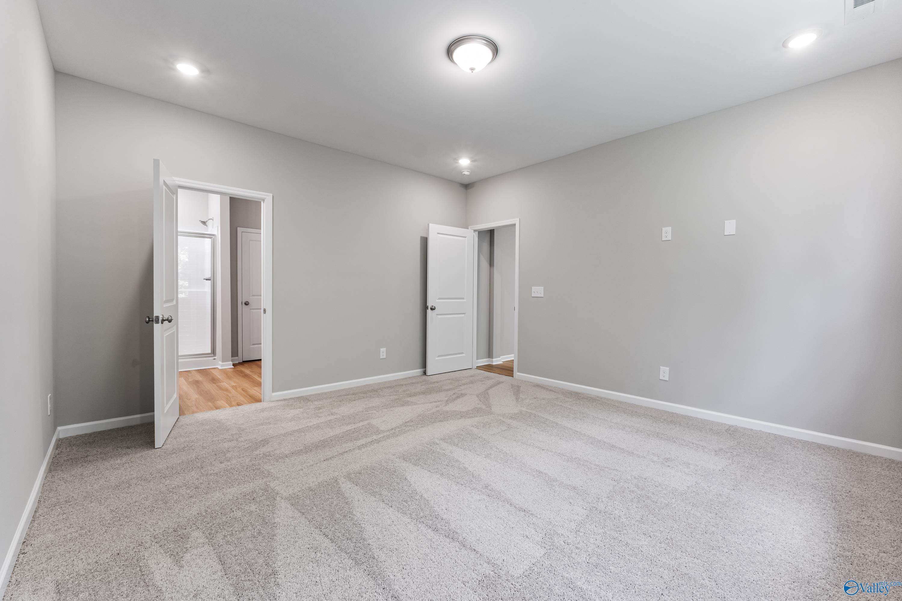 Spacious master bedroom with gray walls, beige carpet, en-suite bath door in The Phoenix 3-bed home, Hazel Green, AL