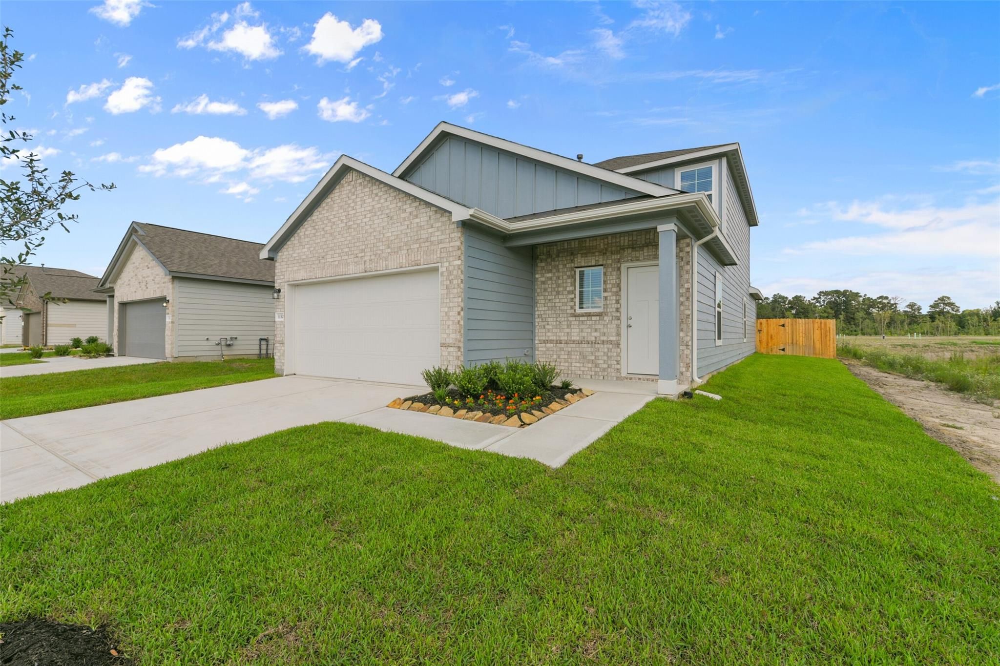 Two-story gray Sabine F home with brick accents, two-car garage, and landscaped yard in The Villages at WestPointe, Dayton, Texas