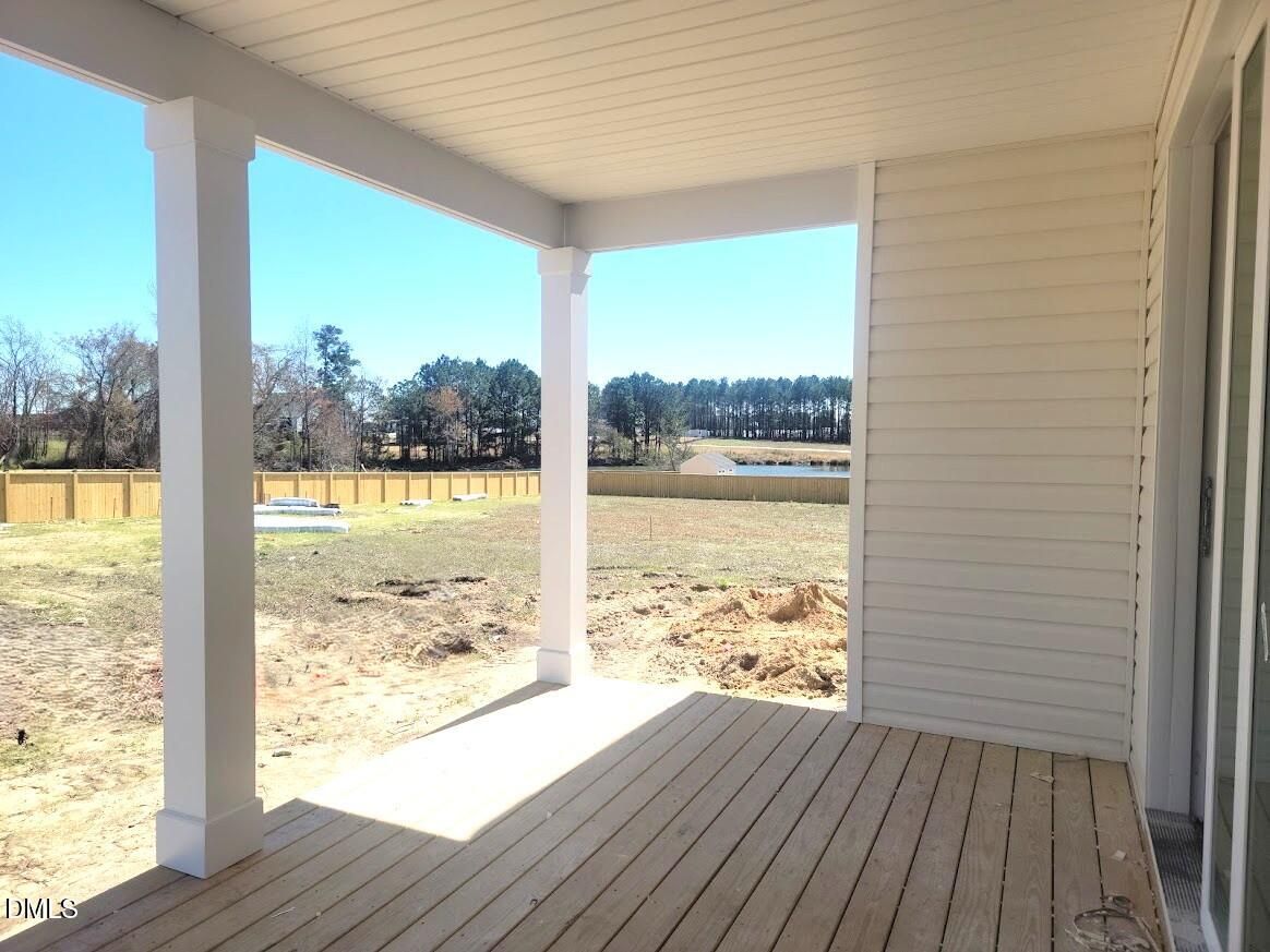 Covered back porch with wooden deck, white columns, and sliding doors overlooking fenced yard in Davidson Homes The Cypress B II, Angier, NC