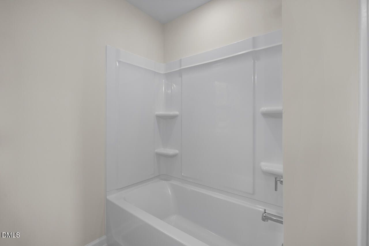 White tub and shower surround with built-in shelving in bathroom at Woodland Crossing by Davidson Homes, Zebulon, NC