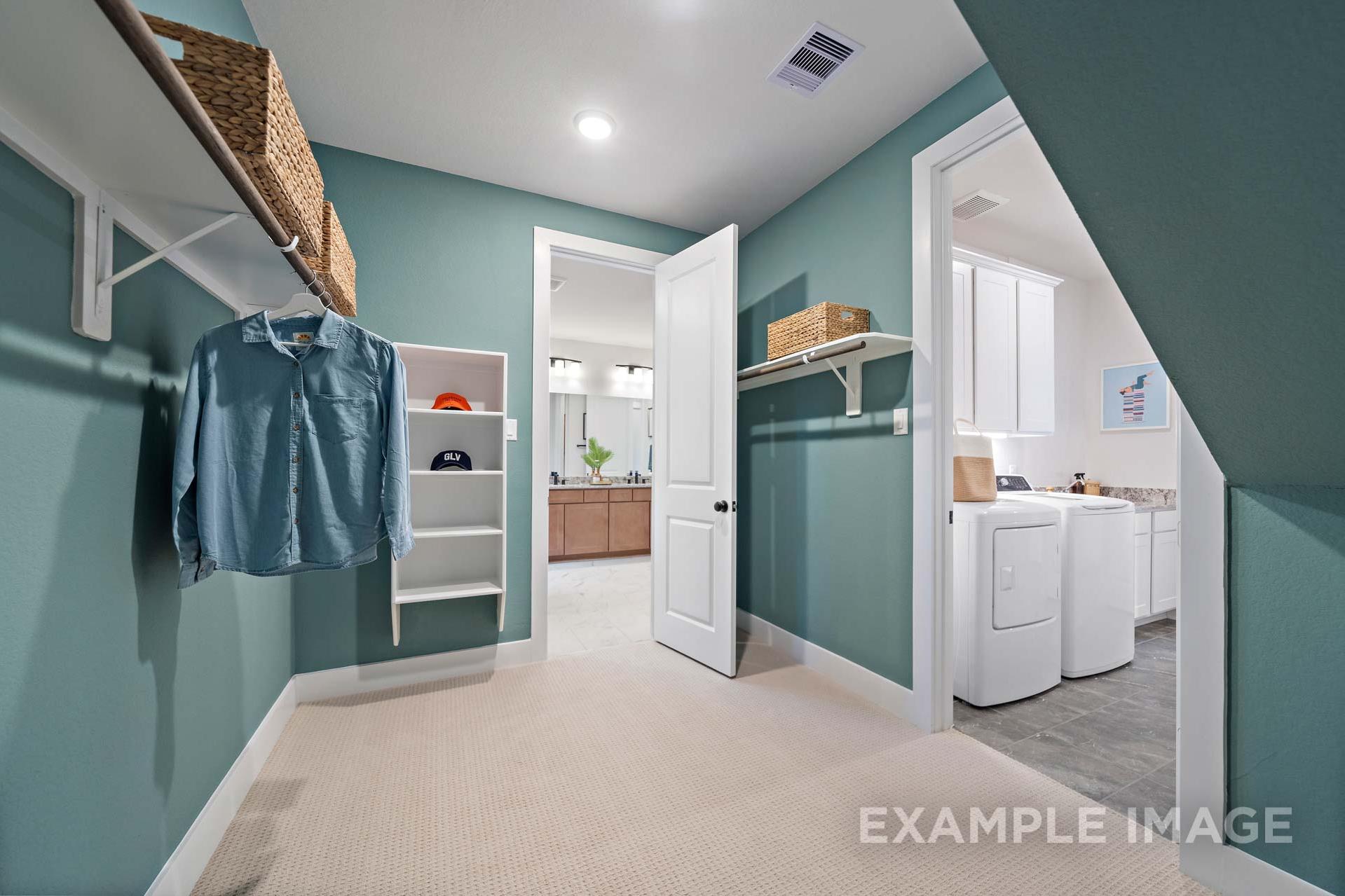 Spacious teal laundry room in The Edward A home with built-in shelves, hanging storage, washer-dryer, and master bath access