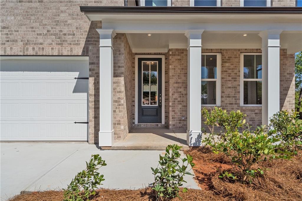 Brick home exterior with covered porch, white columns, dark door, 3-car garage in Davidson Homes Hickory E, Buford, GA
