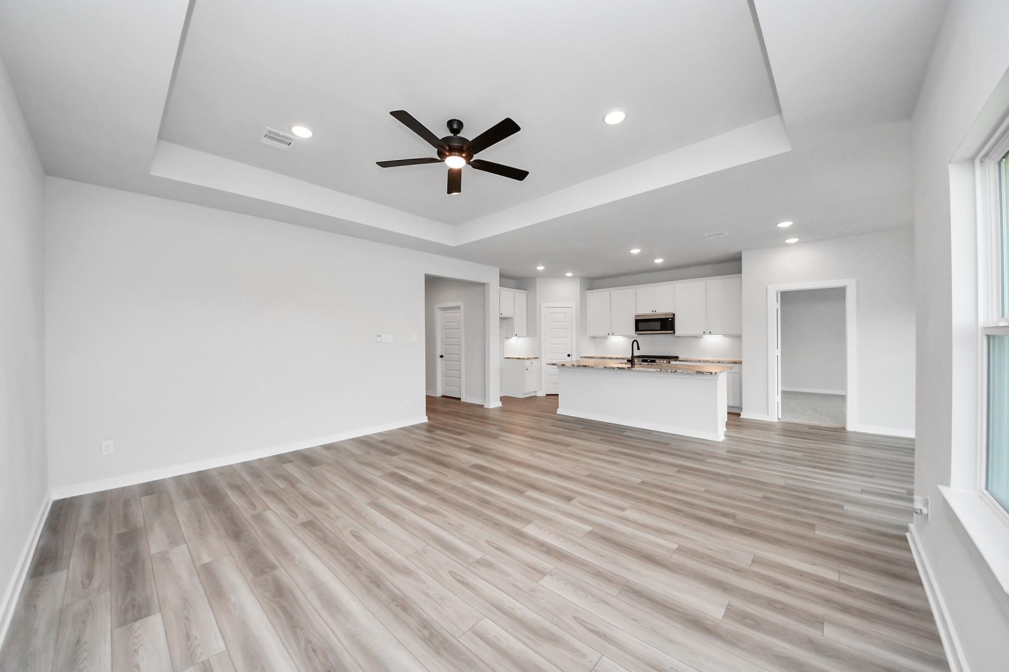 Open-concept living room and kitchen with tray ceiling in The Everett C floor plan at River Ranch Meadows in Dayton, TX.