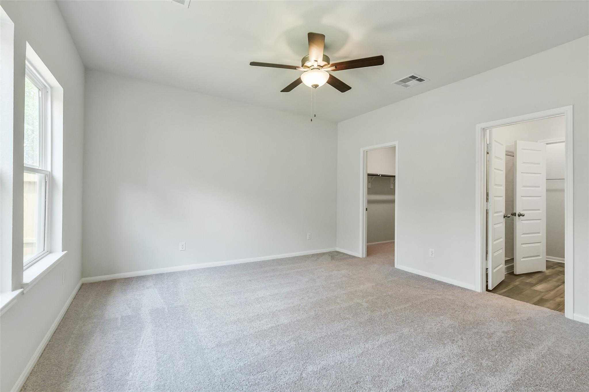 Bright master bedroom with ceiling fan, large windows, and walk-in closet in Davidson Homes The Sabine E, Conroe, Texas