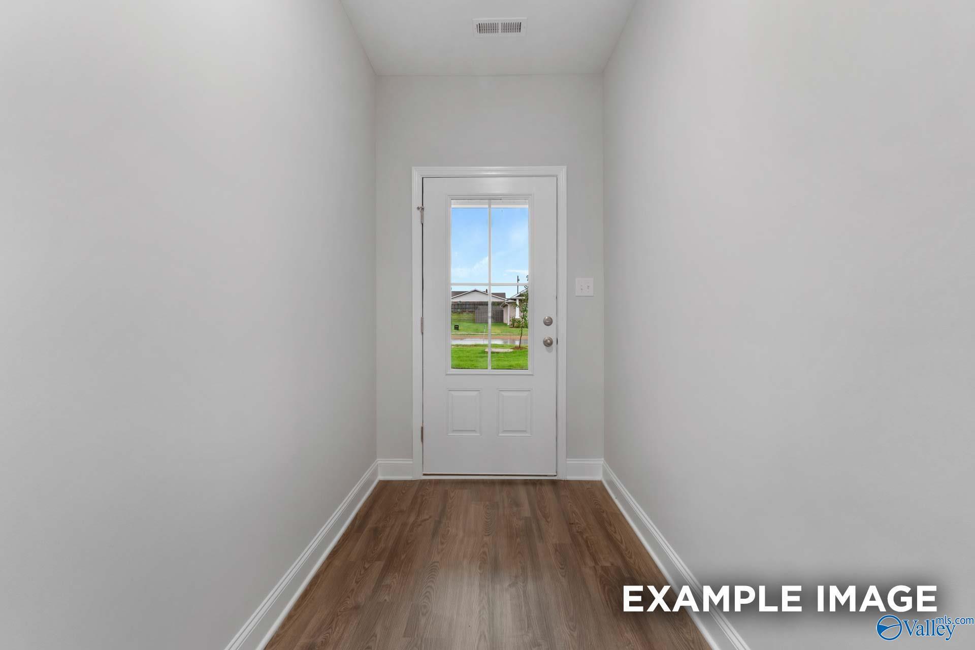 Bright hallway with hardwood floors and white walls leading to glass-paneled back door overlooking lush green yard in Davidson Homes The Cumberland C, Decatur, Alabama