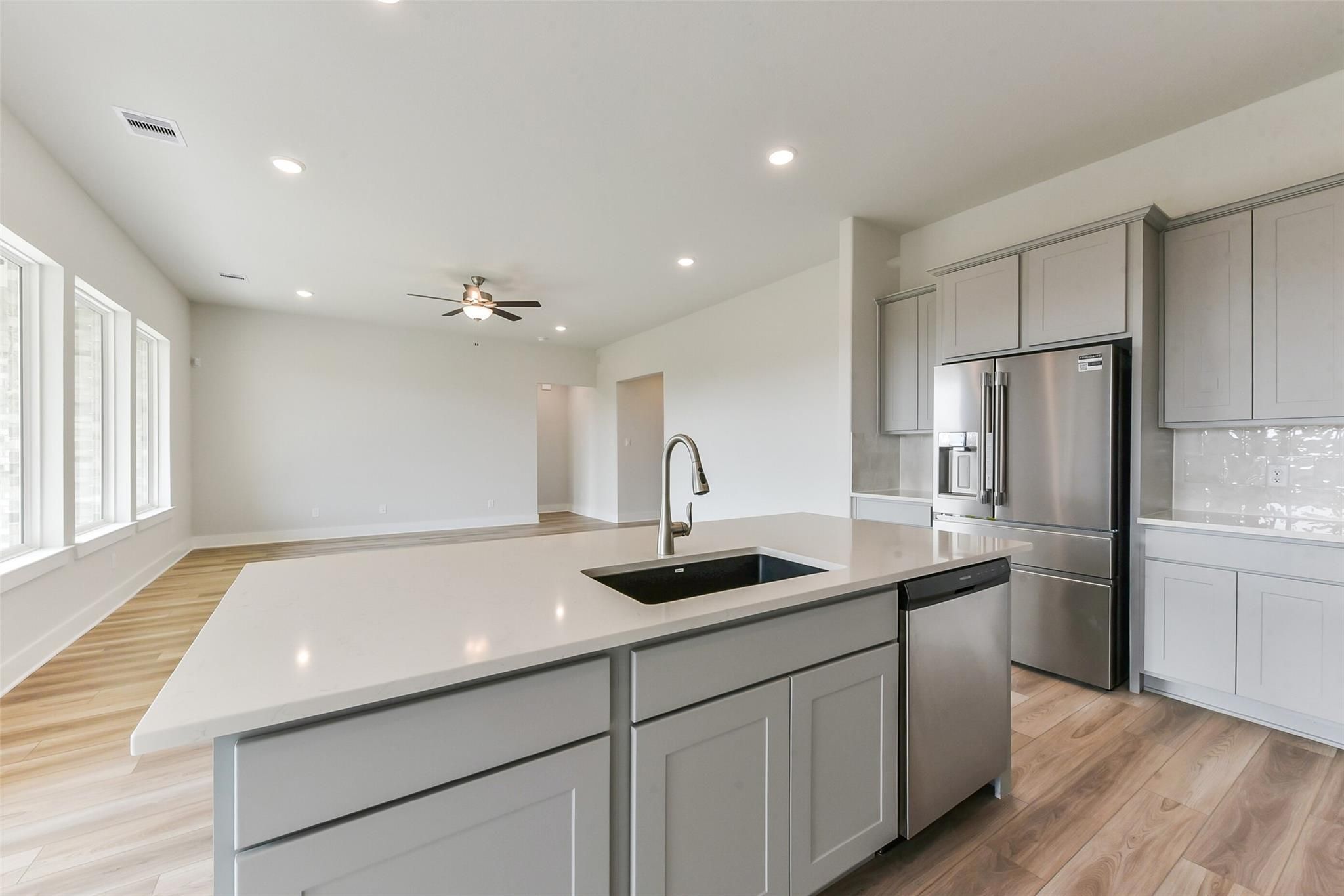 Modern open-concept kitchen with gray shaker cabinets, white quartz island sink, stainless fridge in Davidson Homes Edward A, Texas City