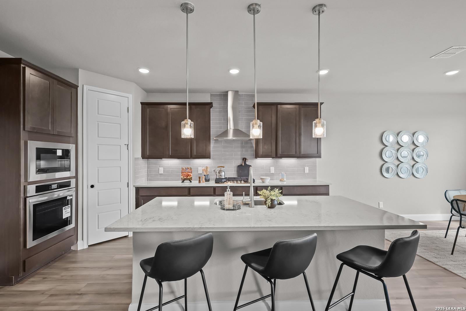Contemporary kitchen with quartz island, stainless double oven, pendant lights in Davidson Homes The Rockford G, Ladera, San Antonio