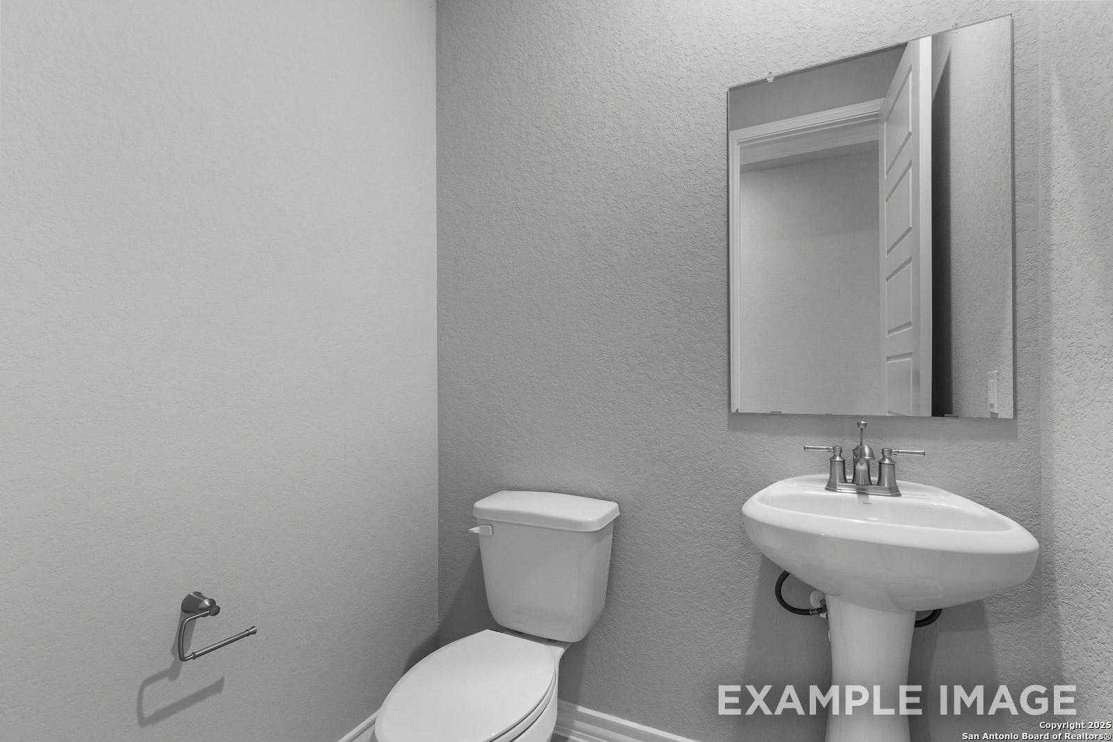 Modern powder room in The Oxford home design featuring a pedestal sink, white toilet, and wall-mounted mirror.