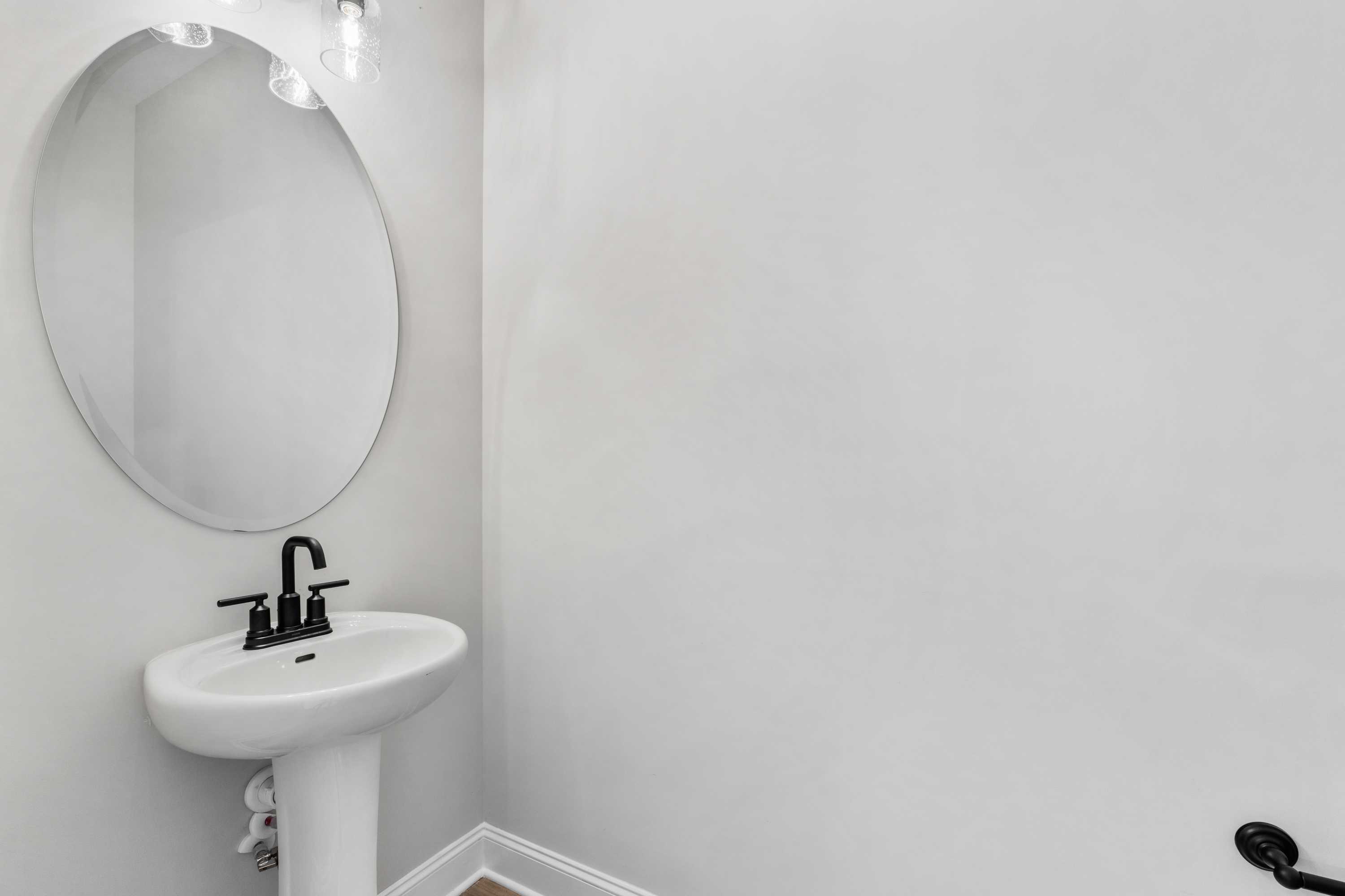 Modern powder room in The Oxford Davidson Homes featuring white pedestal sink, black faucet, and round mirror
