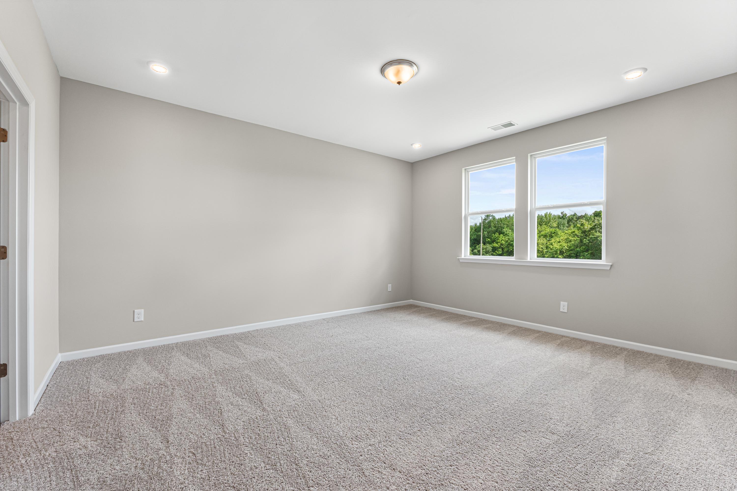 Spacious empty bedroom in The Haven E with light gray walls, beige carpet, dual windows overlooking greenery, recessed ceiling lights