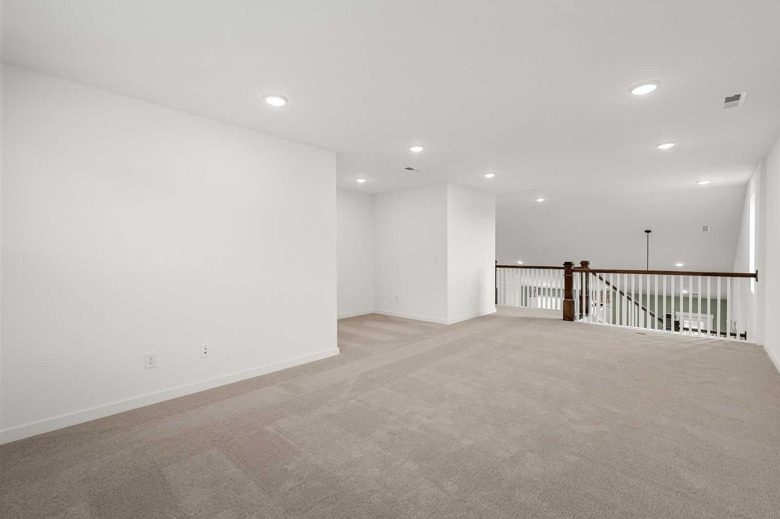 Spacious upstairs loft with wooden railing overlook, beige carpet, and recessed lights in Davidson Homes The Ridgeport, Gallatin, TN