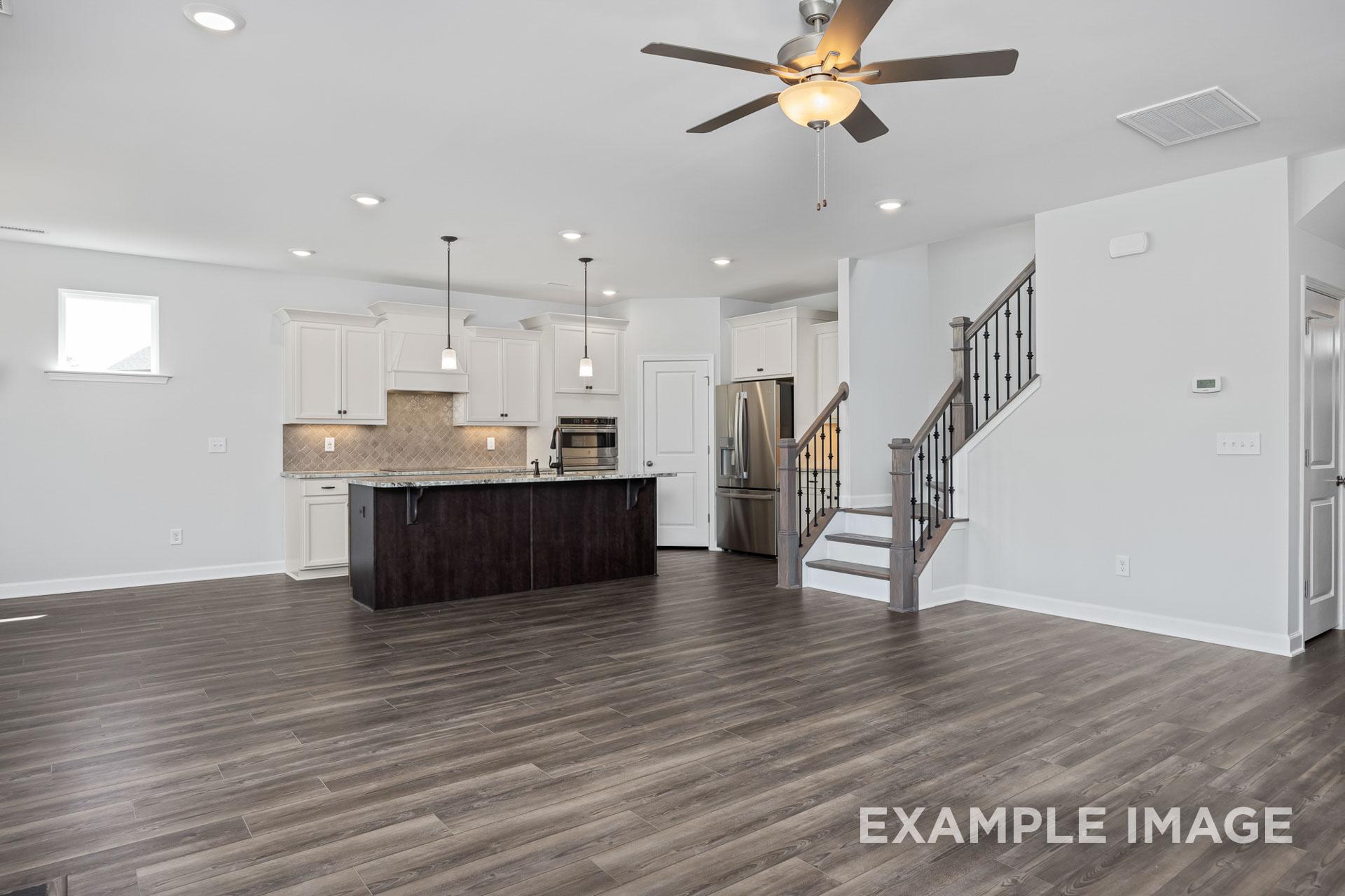Spacious open-concept kitchen and family room in The Grace C with white cabinets, dark island, stainless fridge, ceiling fan, and staircase
