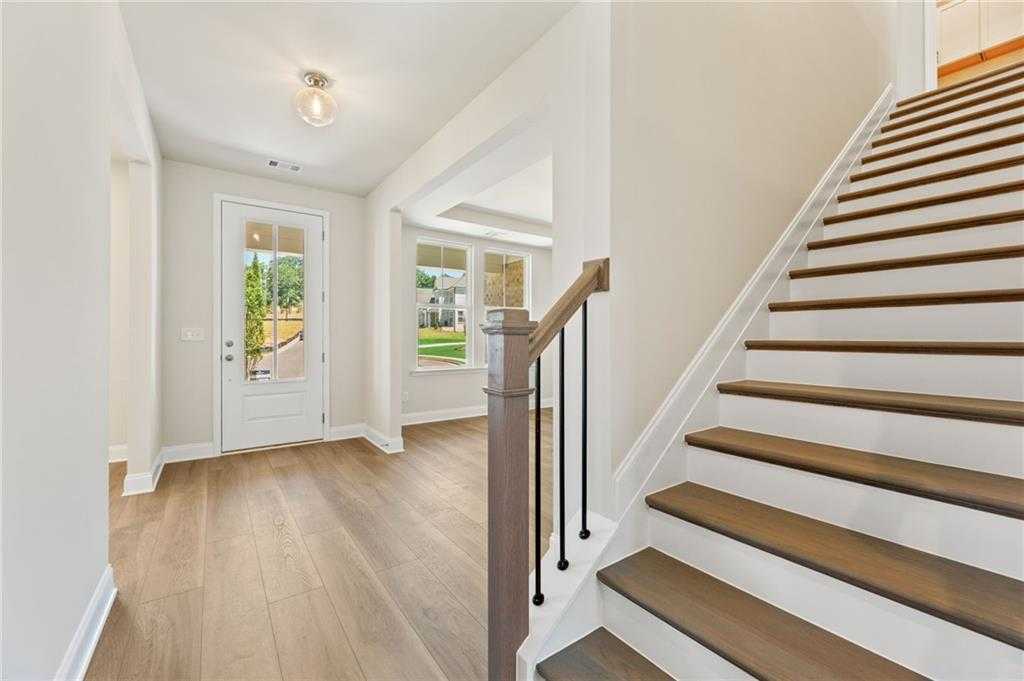 Bright foyer with grand wooden staircase, hardwood floors, and natural light in The Hampton C home, Buford, Georgia