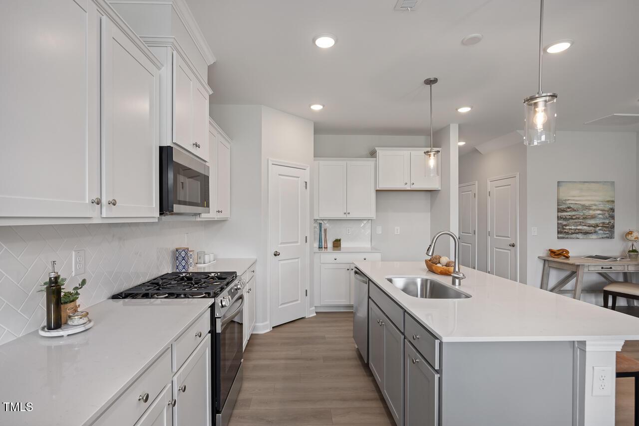 Modern white kitchen with shaker cabinets, stainless appliances, subway tile backsplash, and large island in Davidson Homes The Warren, Fuquay-Varina, NC