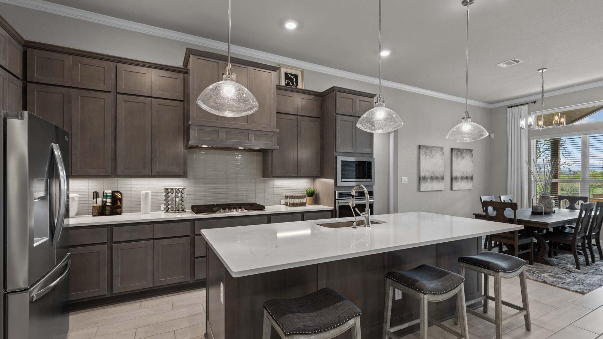 Spacious modern kitchen at Ladera in San Antonio TX with dark cabinets, white quartz island, bar stools, and adjacent dining area