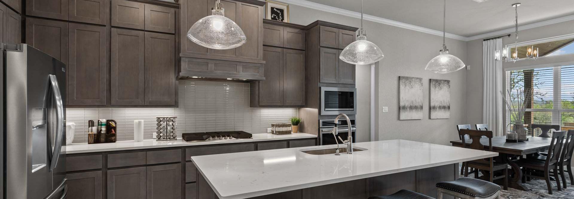 Spacious modern kitchen at Ladera in San Antonio TX with dark cabinets, white quartz island, bar stools, and adjacent dining area