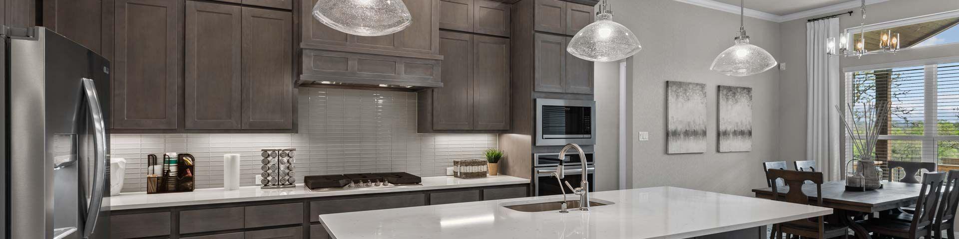 Spacious modern kitchen at Ladera in San Antonio TX with dark cabinets, white quartz island, bar stools, and adjacent dining area