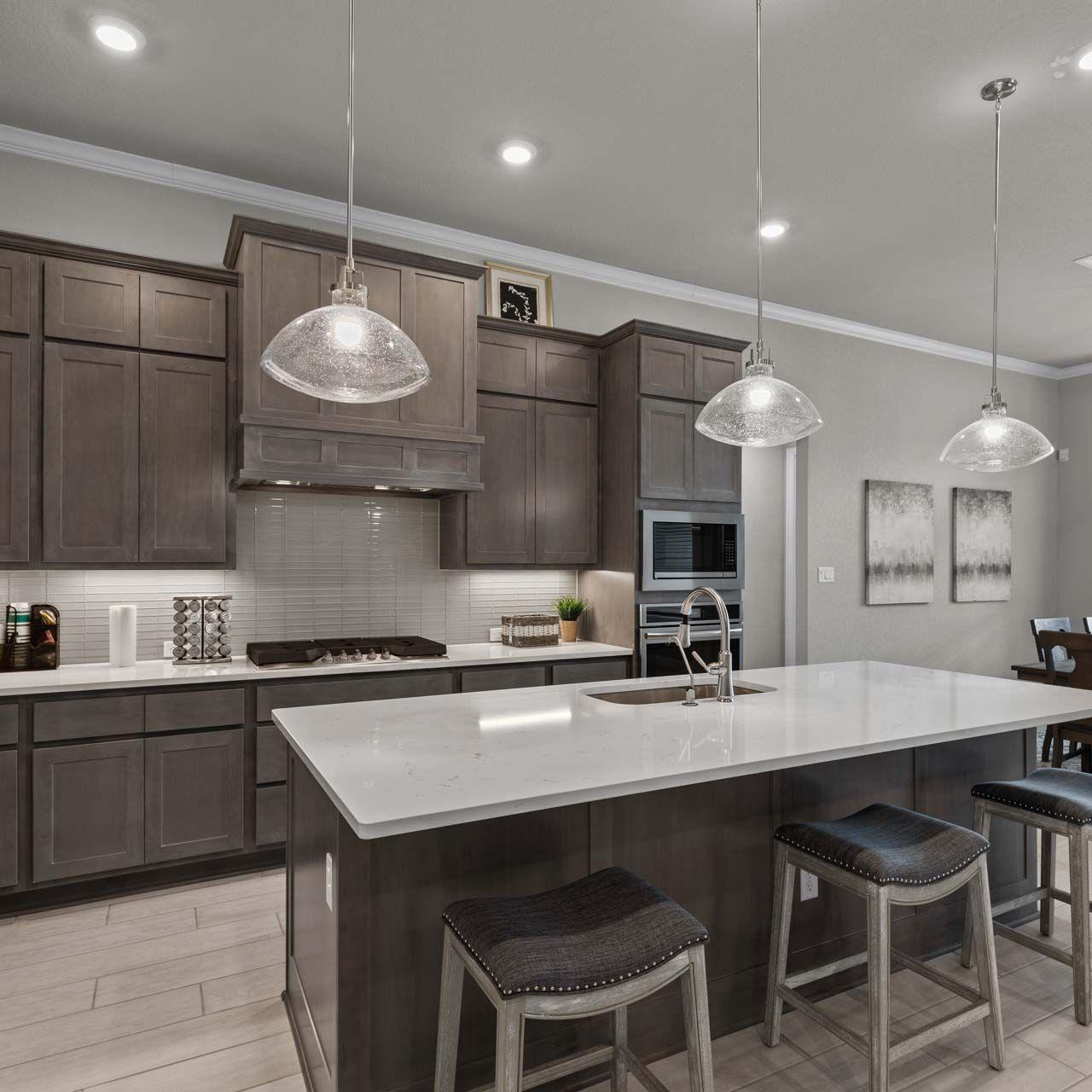 Spacious modern kitchen at Ladera in San Antonio TX with dark cabinets, white quartz island, bar stools, and adjacent dining area