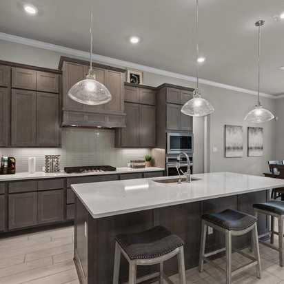 Spacious modern kitchen at Ladera in San Antonio TX with dark cabinets, white quartz island, bar stools, and adjacent dining area