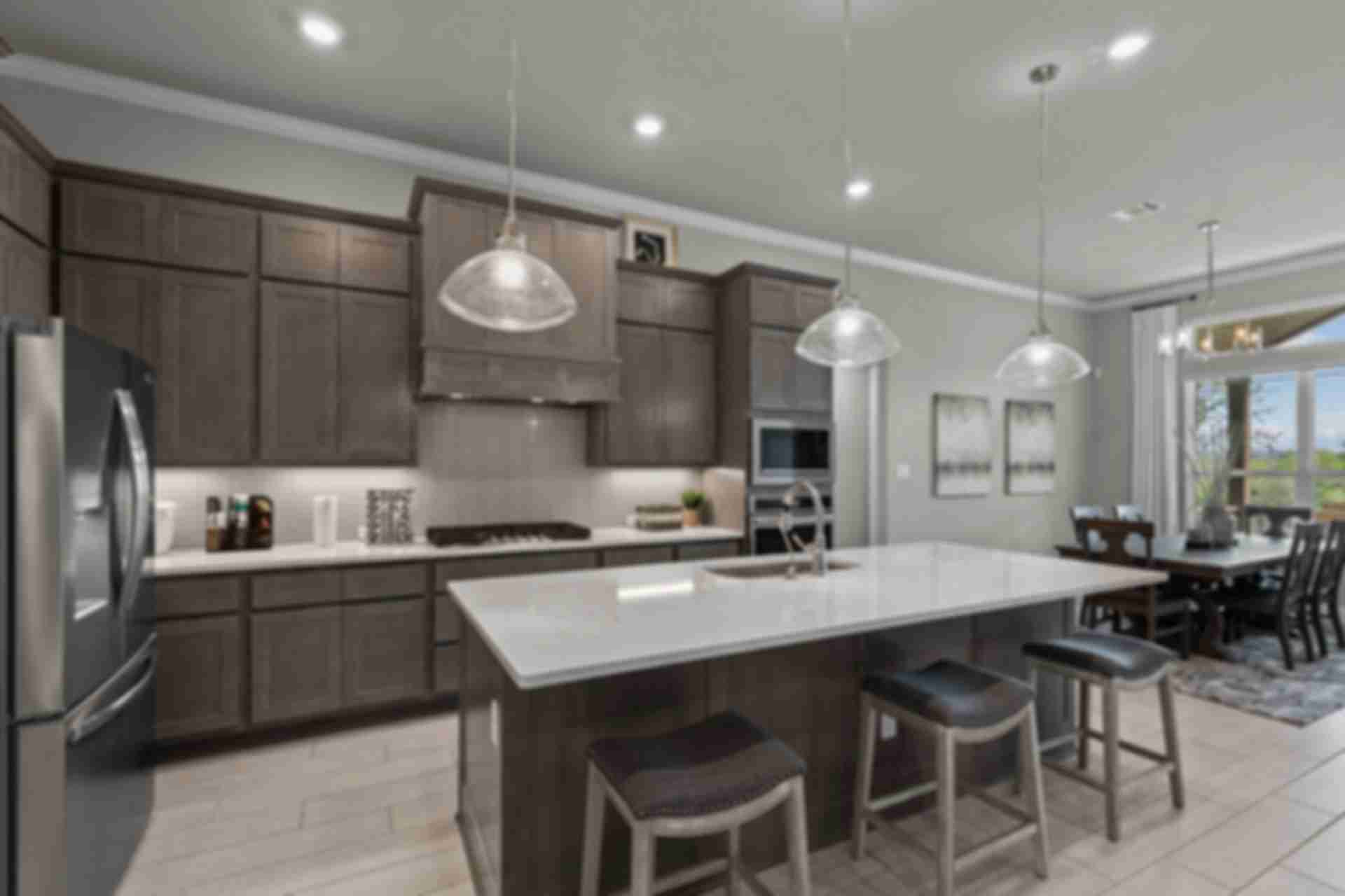 Spacious modern kitchen at Ladera in San Antonio TX with dark cabinets, white quartz island, bar stools, and adjacent dining area