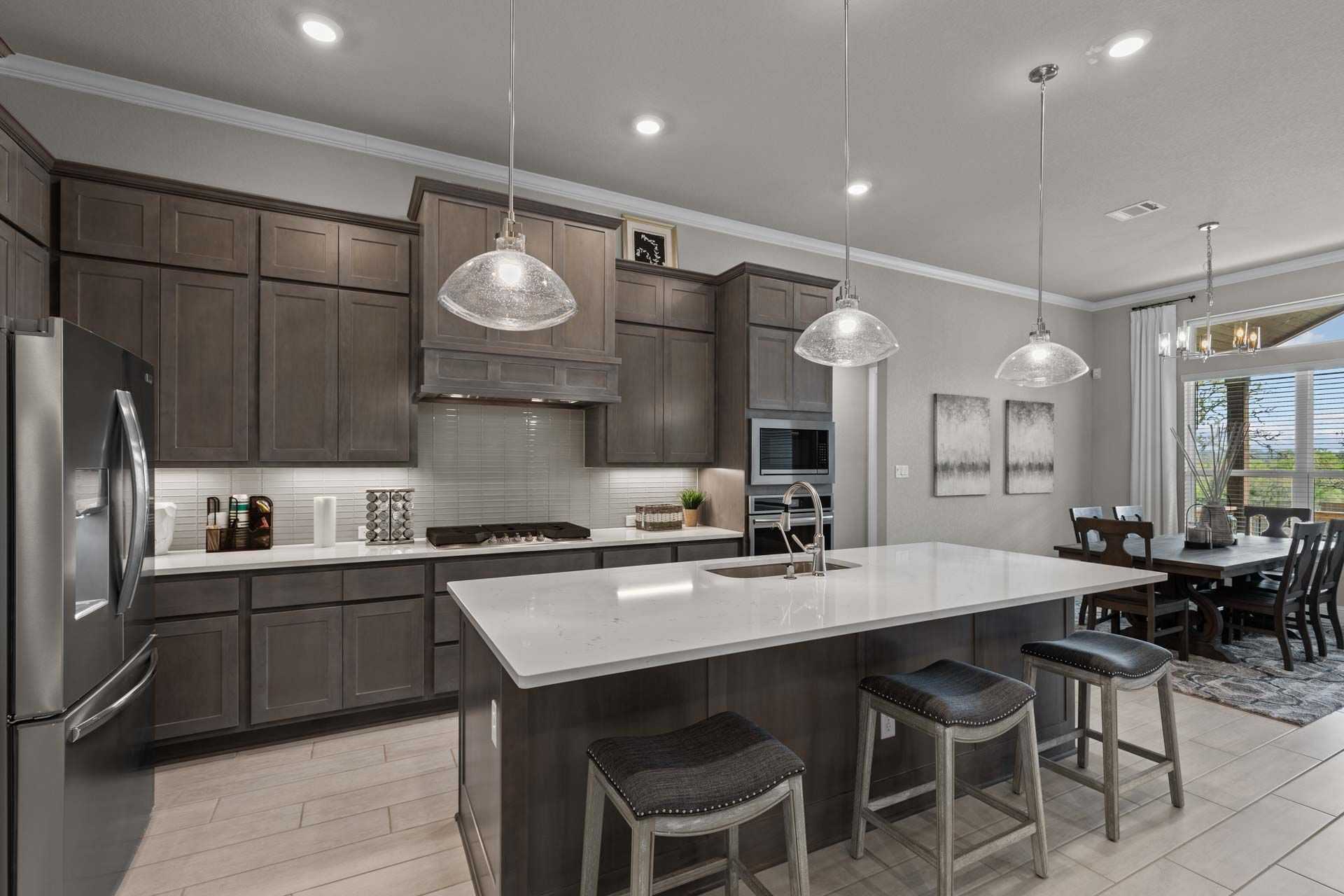 Modern kitchen in Ladera San Antonio by Davidson Homes with dark shaker cabinets, white quartz island, bar stools, and pendant lights