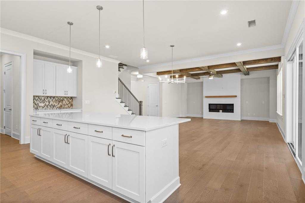 Spacious open-concept kitchen with white island, tile backsplash, and living area with wood beams, fireplace in Davidson Homes The Arlington A, East Cobb
