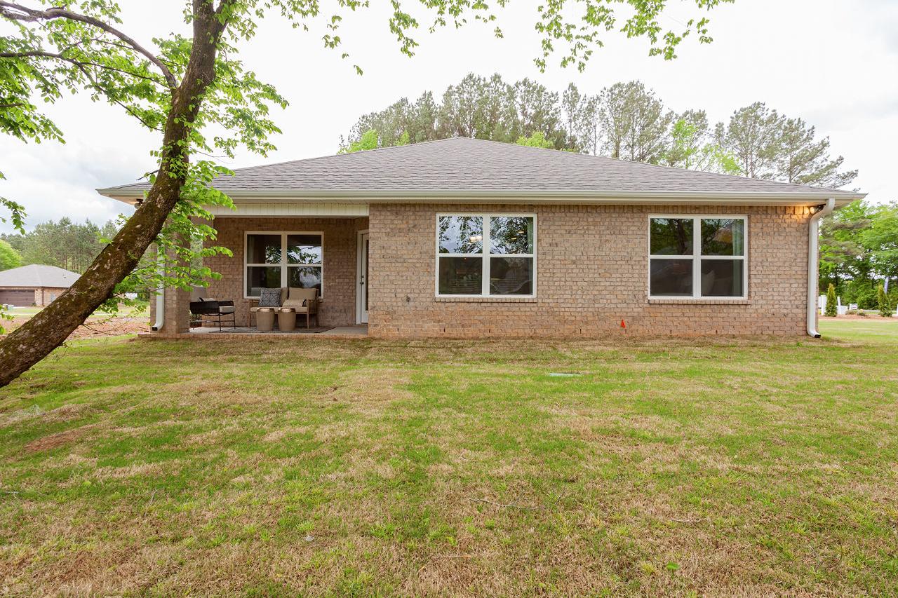 Rear view of The Franklin 3-bedroom single-family home with brick exterior, covered patio, large windows, and lush green yard in Meridianville AL