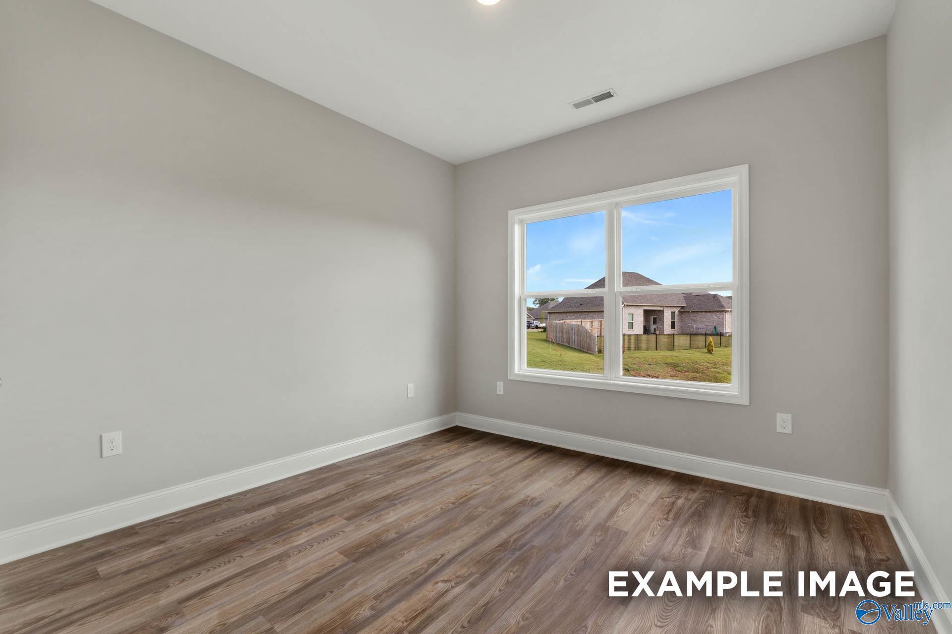 Bright secondary bedroom with gray walls, hardwood floors, and large window overlooking fenced backyard in The Shelby B, New Market, AL
