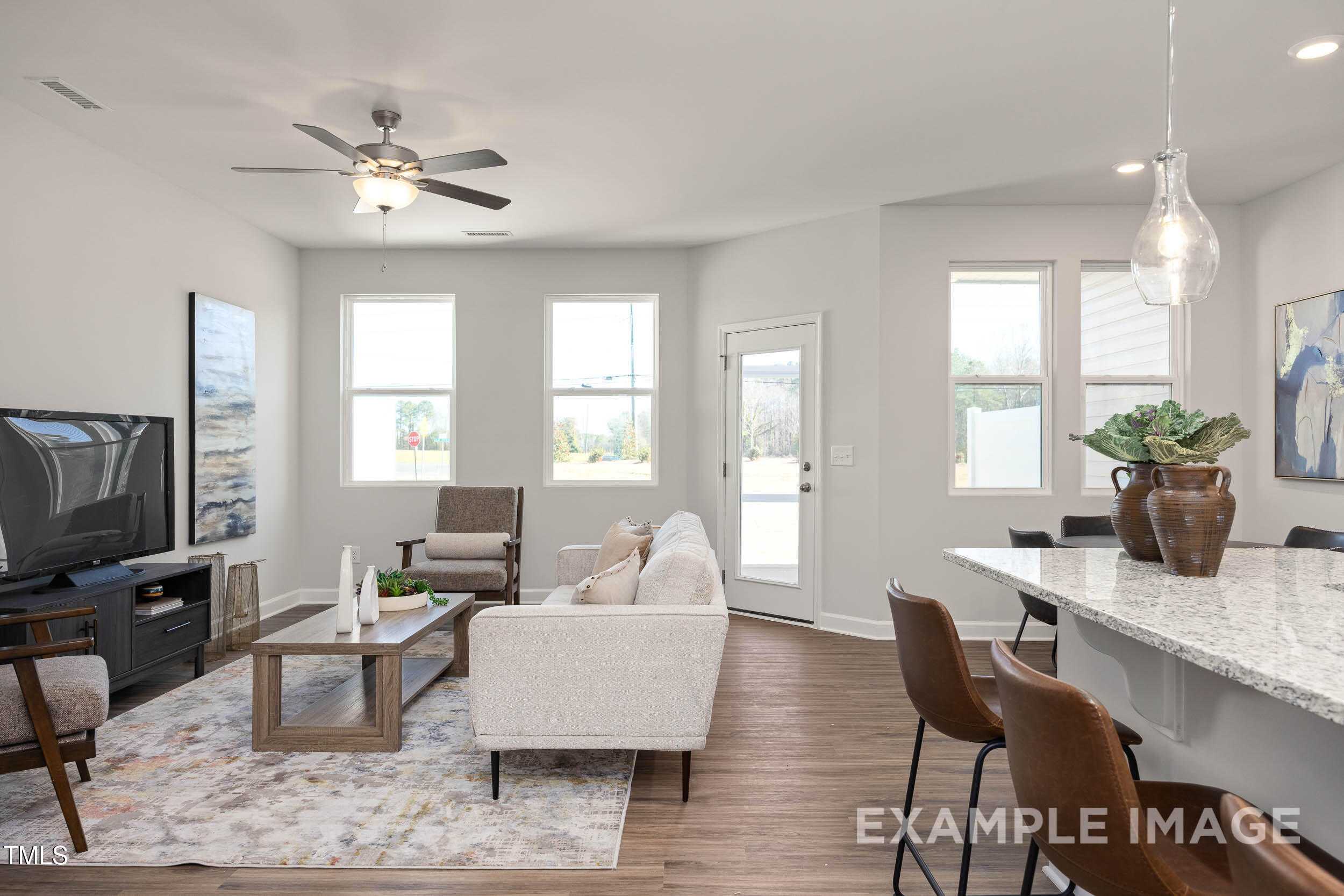 Open-concept living room with beige sofa, TV, ceiling fan, and kitchen island in Davidson Homes The Graham, Fuquay-Varina, NC