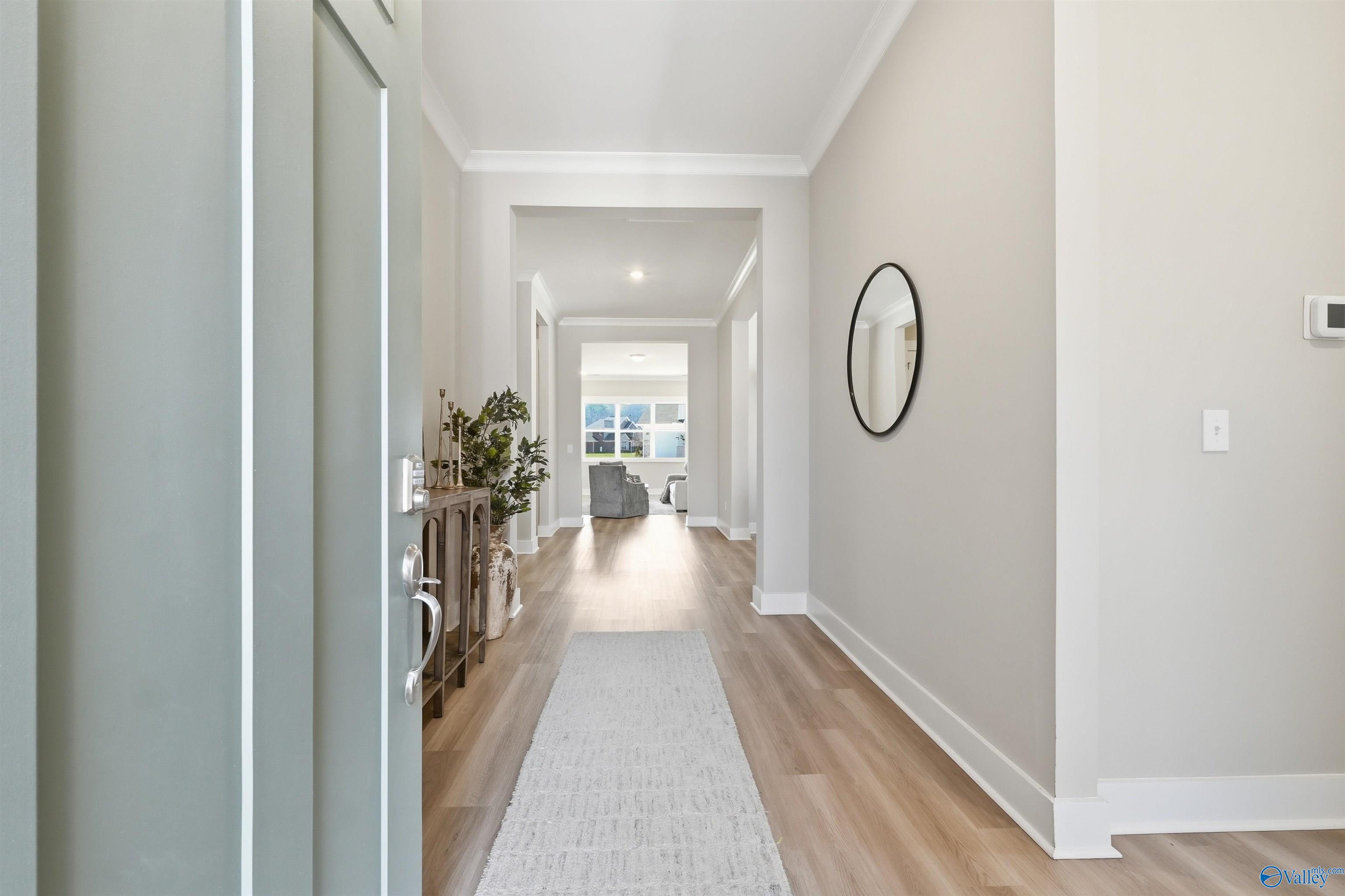 Welcoming entry hallway with light oak floors, beige walls, round mirror, and console table in Evermore Homes The Oxford B, Owens Cross Roads, Alabama
