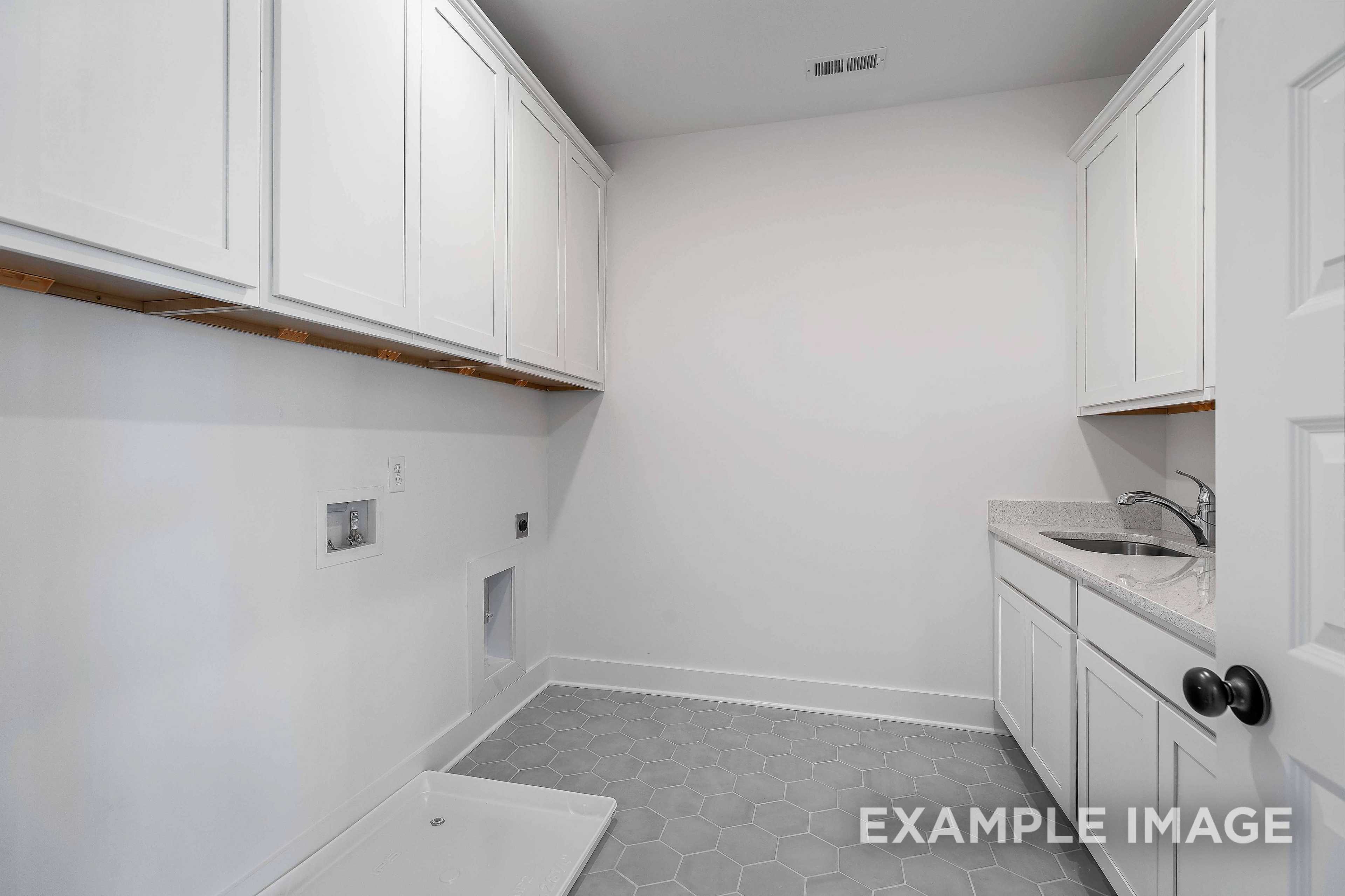 Spacious laundry room in The Albany A home with white cabinets, utility sink, washer-dryer hookups, open shelves, and gray tile floor