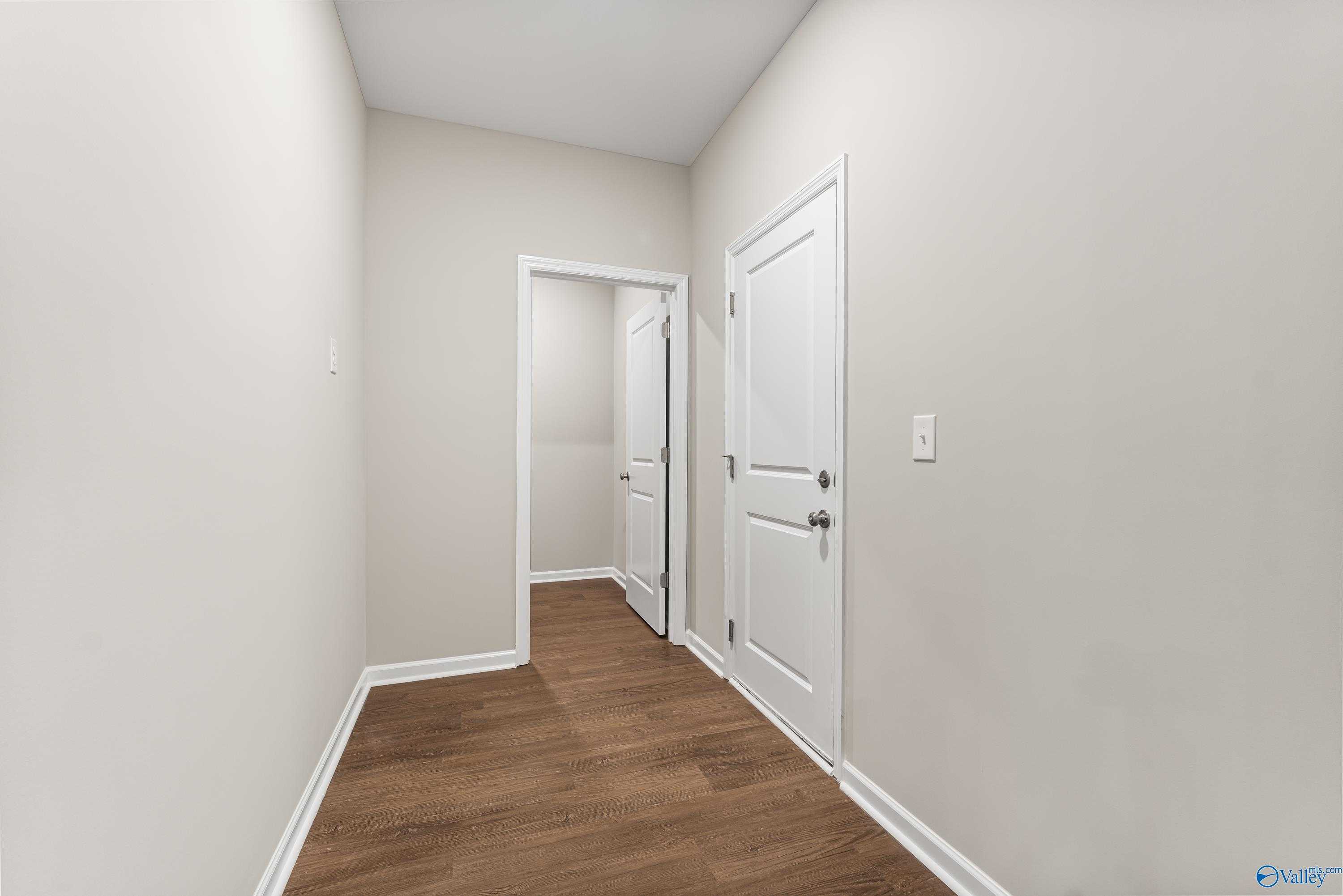 Bright hallway with hardwood floors, beige walls, and white doors in 3-bedroom The Phoenix home by Davidson Homes, Fayetteville, TN
