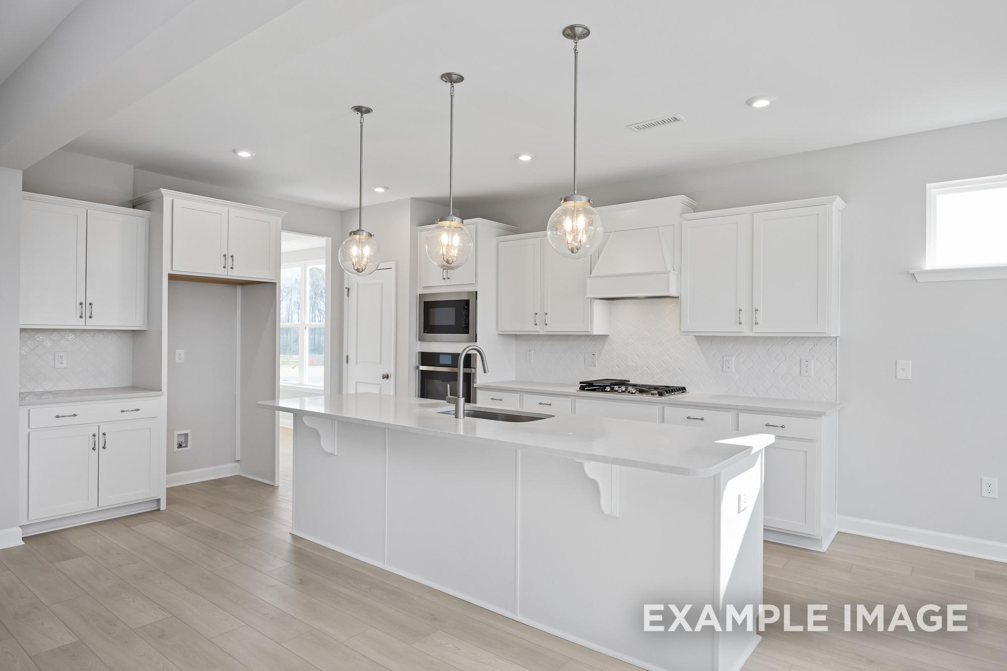 Spacious white kitchen in The Cypress B II by Davidson Homes featuring large island, pendant lights, and stainless appliances