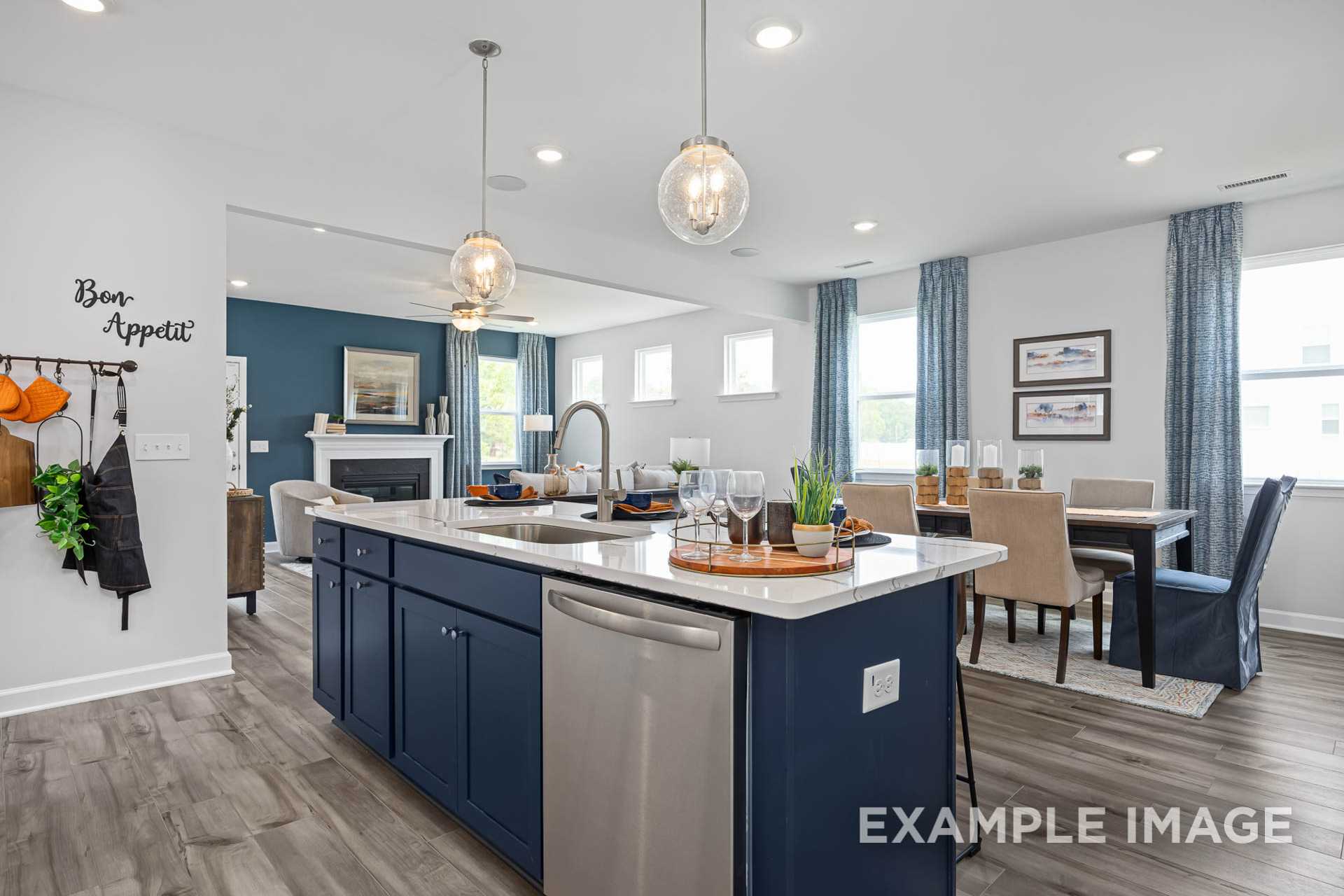 Open-concept kitchen in The Adalynn A with navy island, stainless appliances, and adjacent dining area