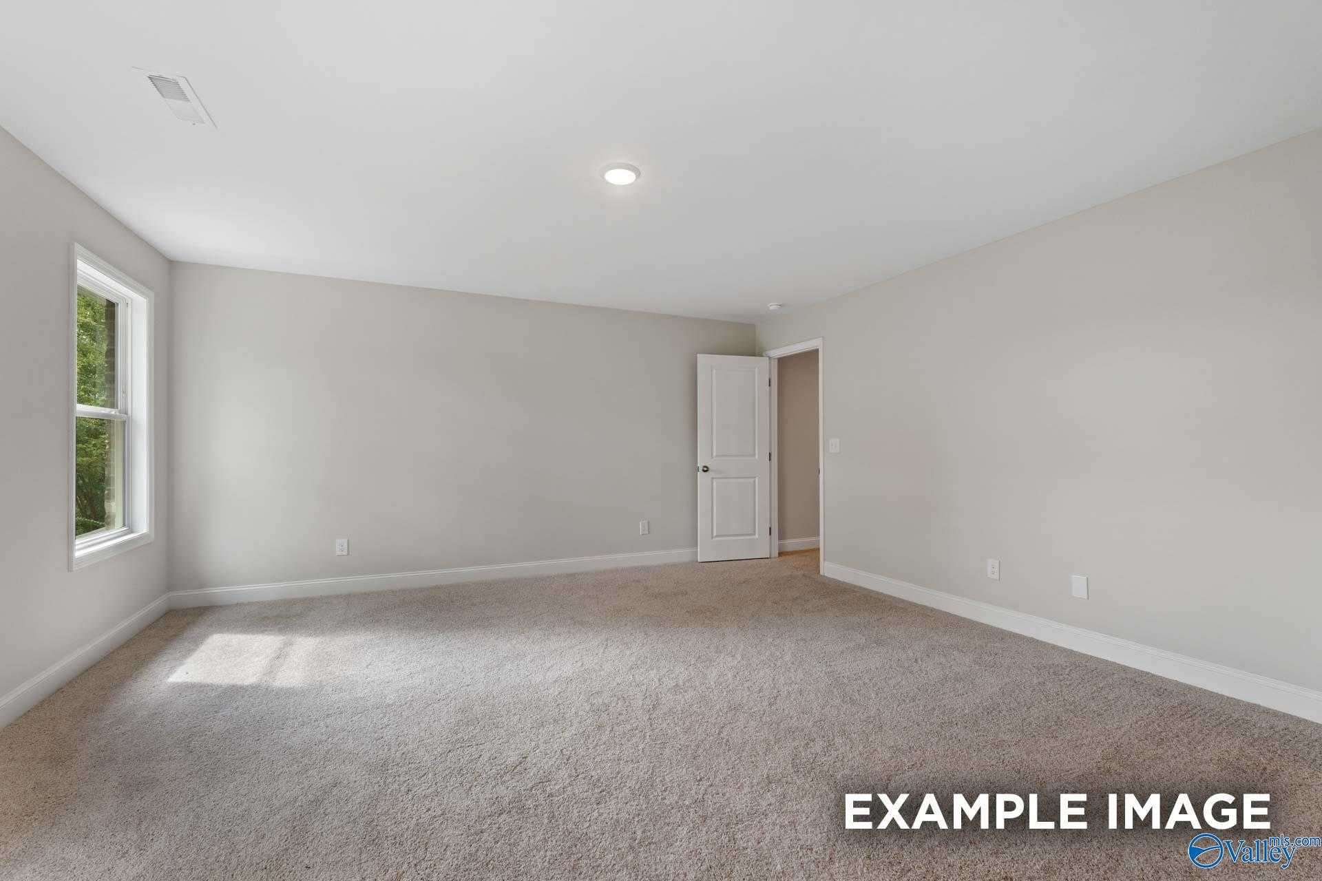 Sunlit empty bedroom with neutral walls, beige carpet, and large window in Davidson Homes The Camden, Huntsville AL