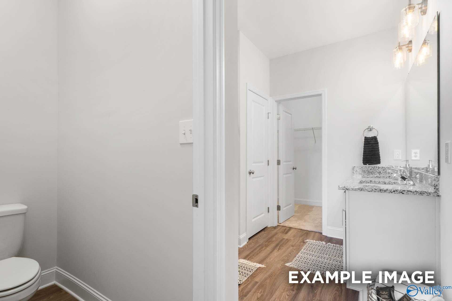 Modern bathroom featuring granite vanity, lighted mirror, toilet, open closet, and hardwood floors in Davidson Homes The Franklin C, Meridianville, Alabama