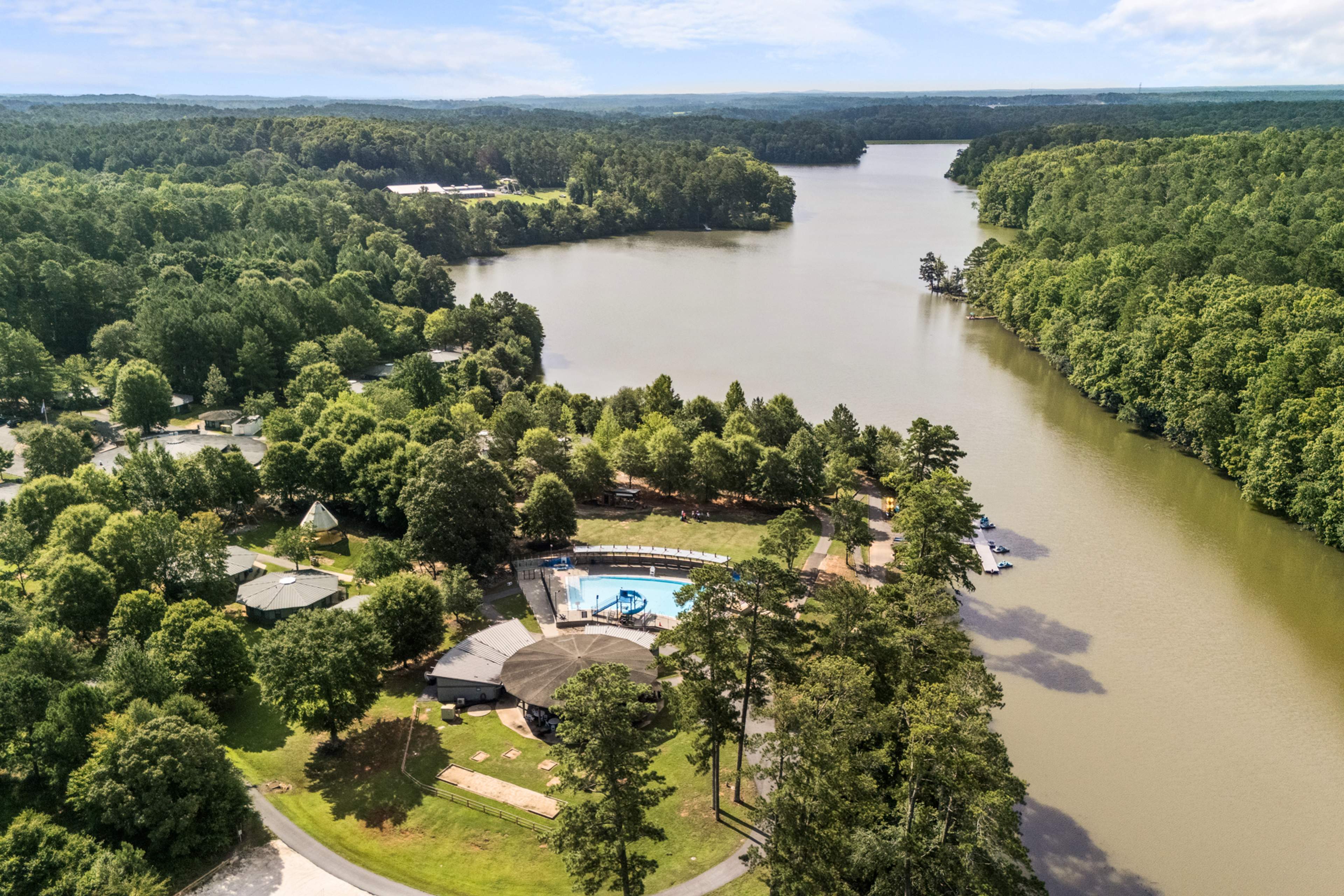 Aerial view of Lake Shore community in Winder GA featuring resort-style pool, clubhouse, lush forest, and serene lakefront