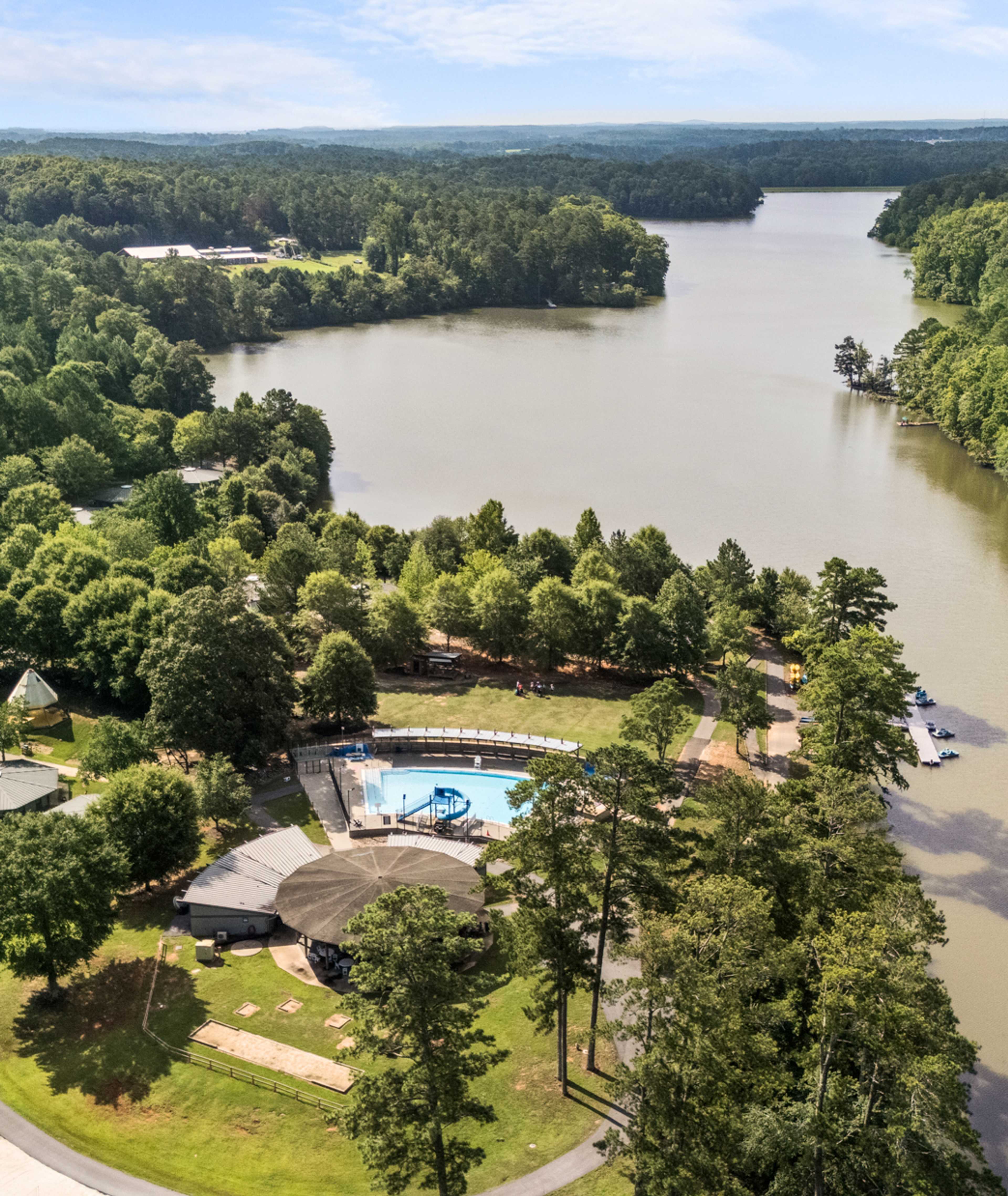 Aerial view of Lake Shore community in Winder GA featuring resort-style pool, clubhouse, lush forest, and serene lakefront