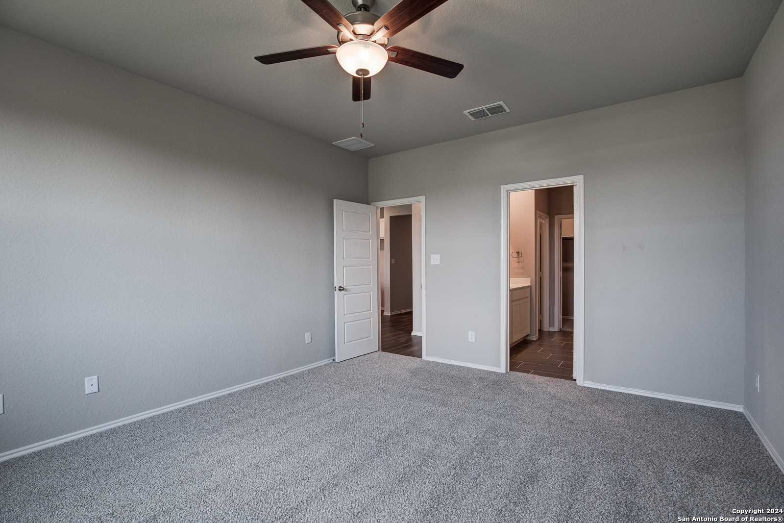 Neutral gray secondary bedroom with ceiling fan, carpet floor, and attached bath vanity in Davidson Homes The Daphne J, Seguin, Texas